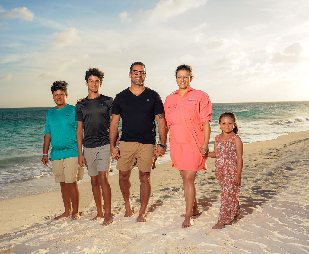 Dr. Revels and family standing barefoot on a sunny beach with ocean waves in the background