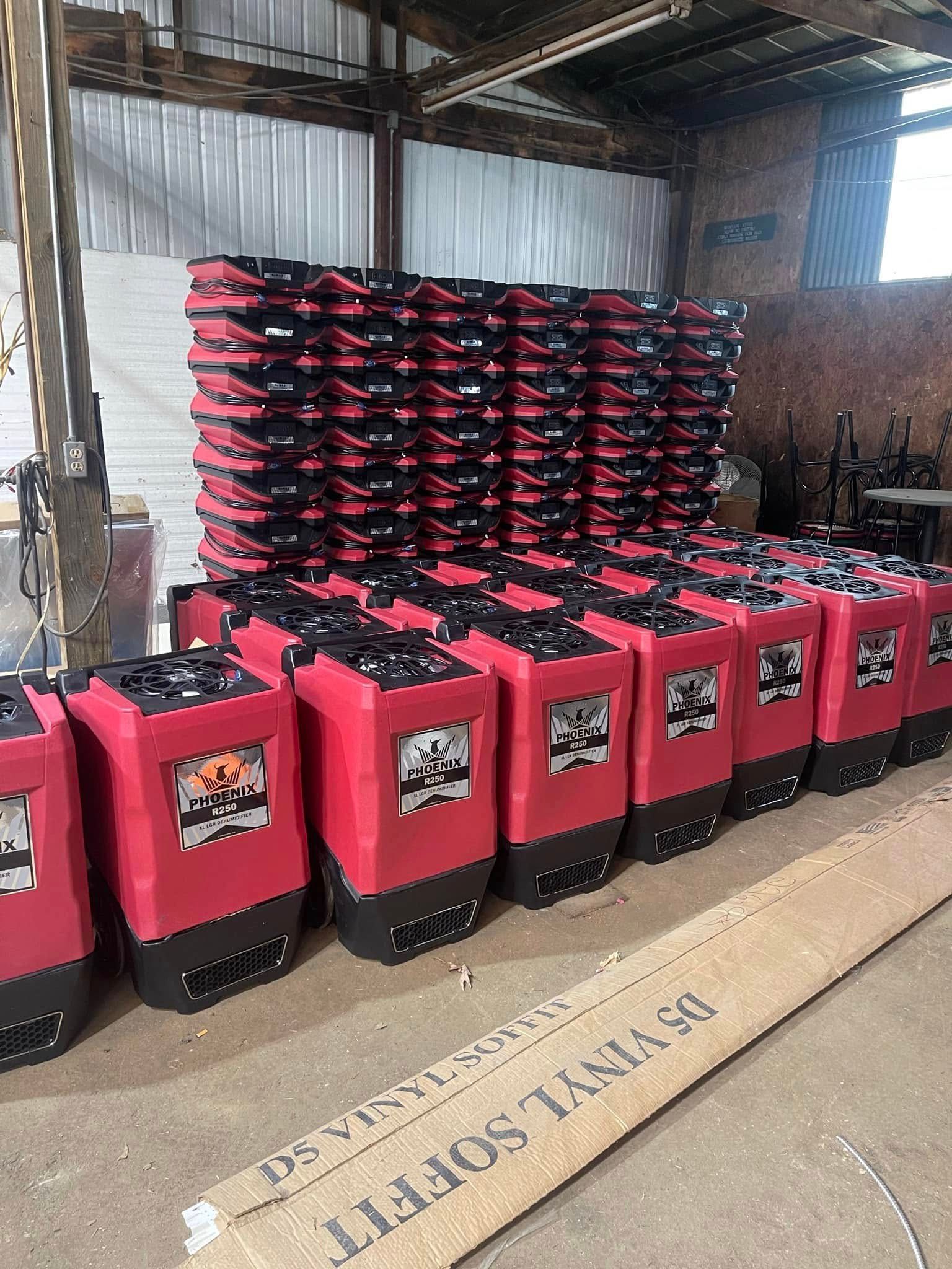 Red and black portable heaters stacked in a warehouse setting, with a cardboard box in the foreground.