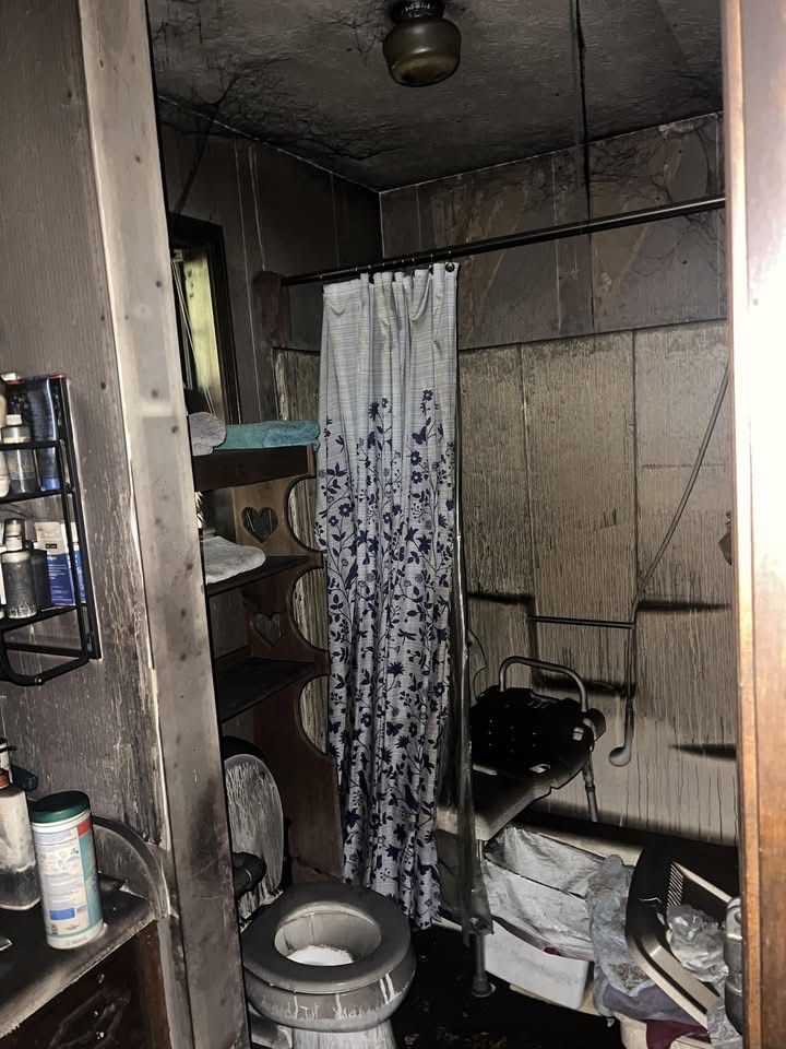 Bathroom interior heavily damaged by fire; walls and ceiling are blackened. Shower curtain hangs.
