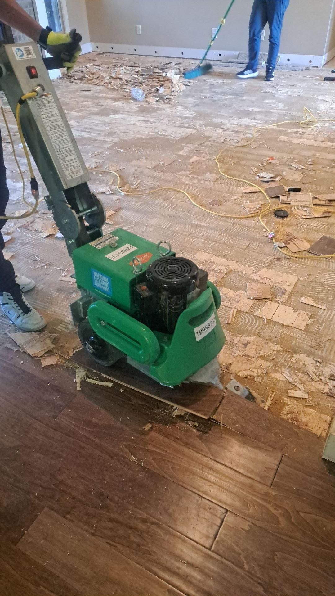 A floor scraper removing dark laminate flooring during renovation, indoors.