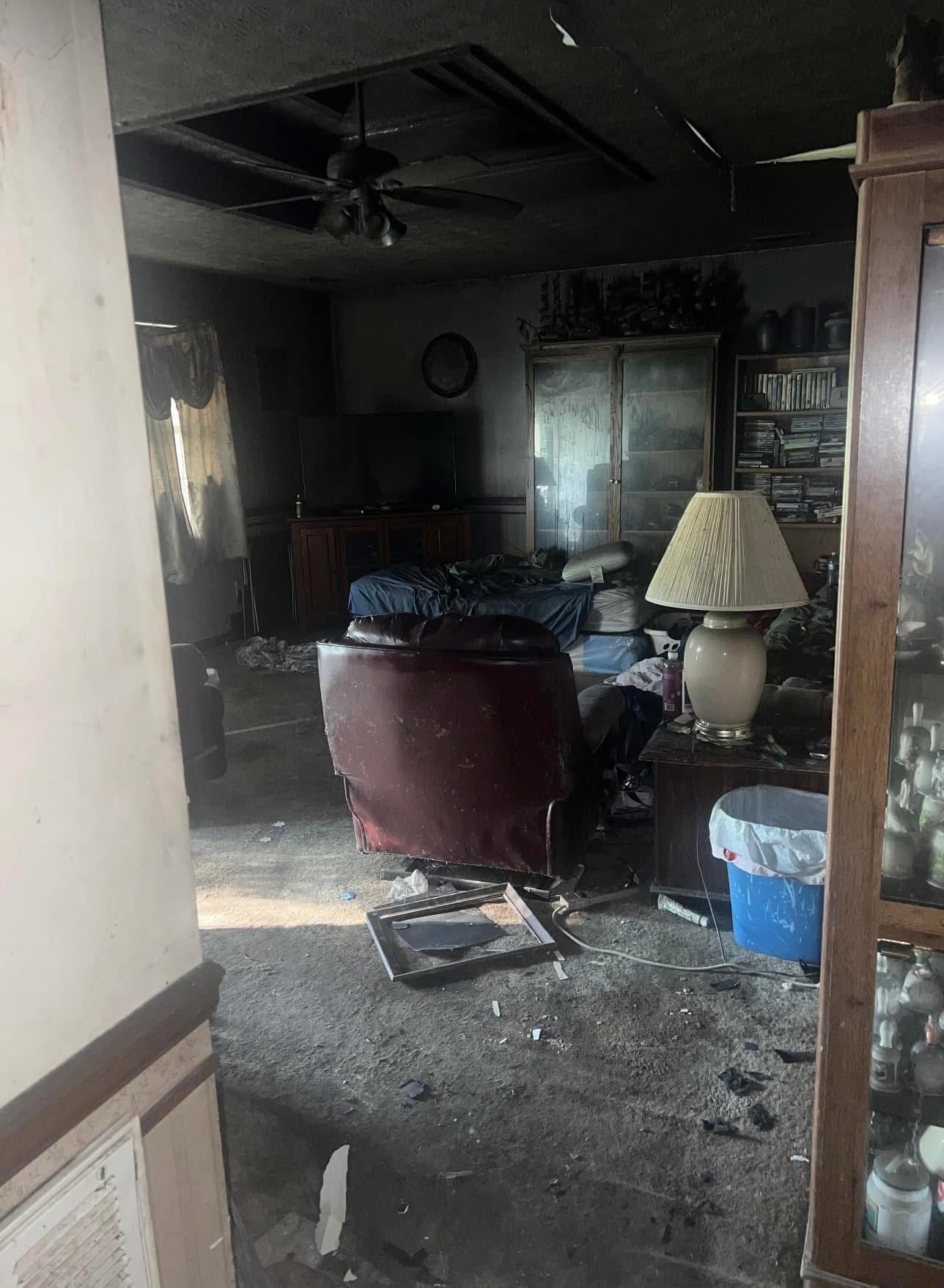 Interior room heavily damaged by fire; charred furniture and debris cover the floor; ceiling and walls are black with soot.