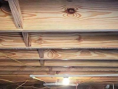 Wooden joists and subflooring in a crawl space, with pipes and wiring visible.
