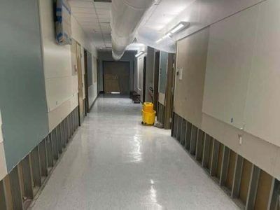 Hallway under construction with exposed metal studs, a yellow bucket, and white walls.
