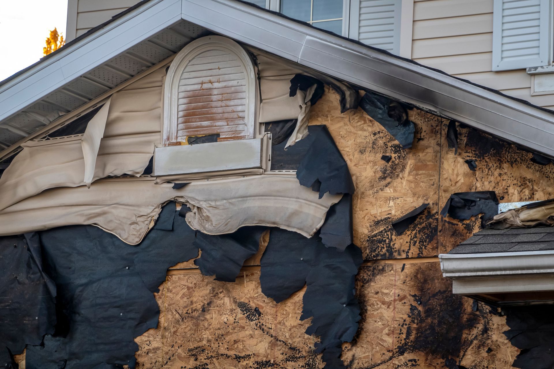 Exterior of a house damaged by fire, charred siding and exposed wood.
