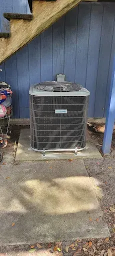 Air conditioning unit on a concrete pad near blue siding and wooden steps.