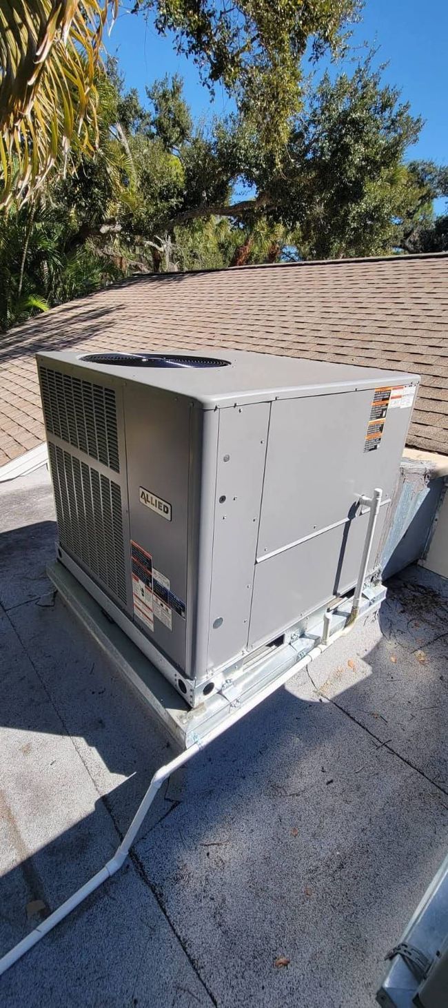 HVAC unit on a rooftop with trees and a clear sky in the background.