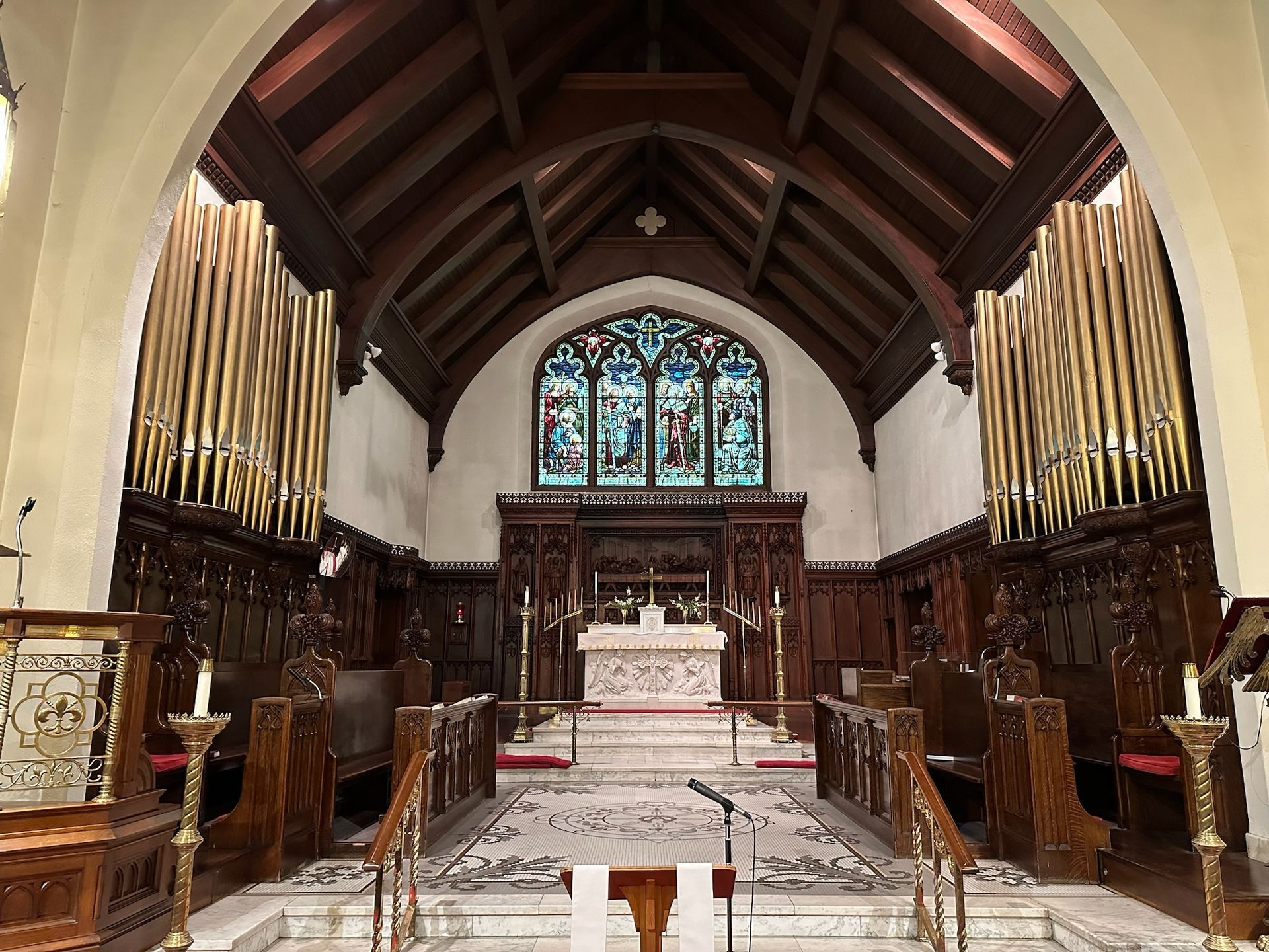 Interior of a church: wooden pews and altar, stained glass window, and gold organ pipes.