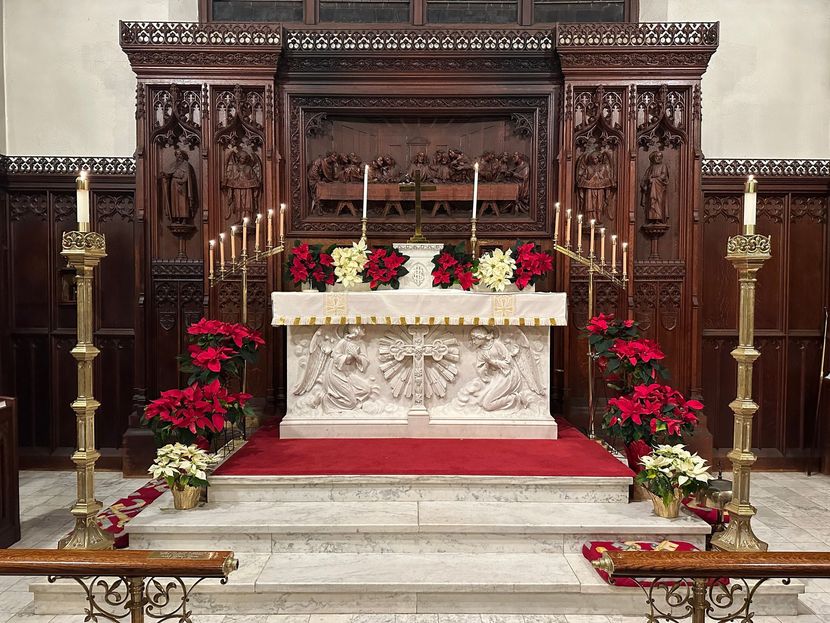 Altar in a church decorated with poinsettias, candles, and a carved wooden backdrop.