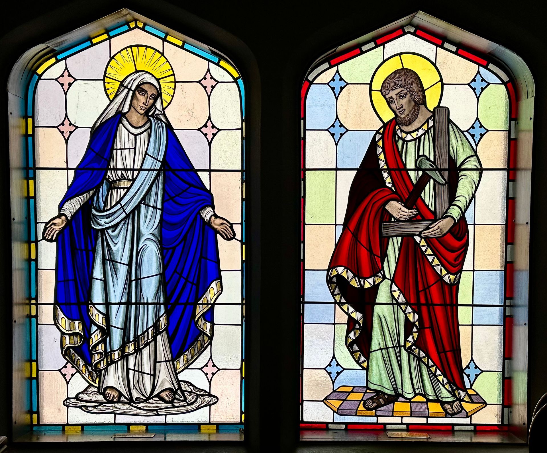 Stained glass windows: Mary in blue robe, halo, and St. Andrew with cross and red mantle.