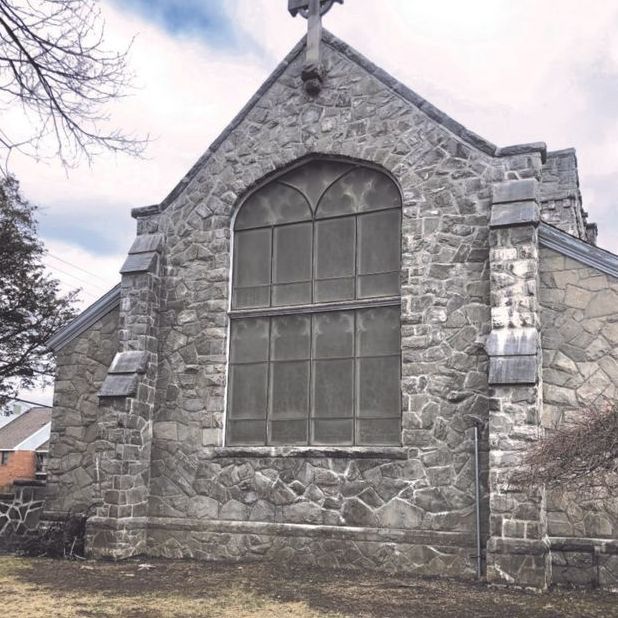 Stone church building with arched window and cross on the roof.