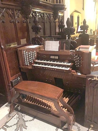 Church organ with multiple keyboards and pedals, in a wood-paneled setting.