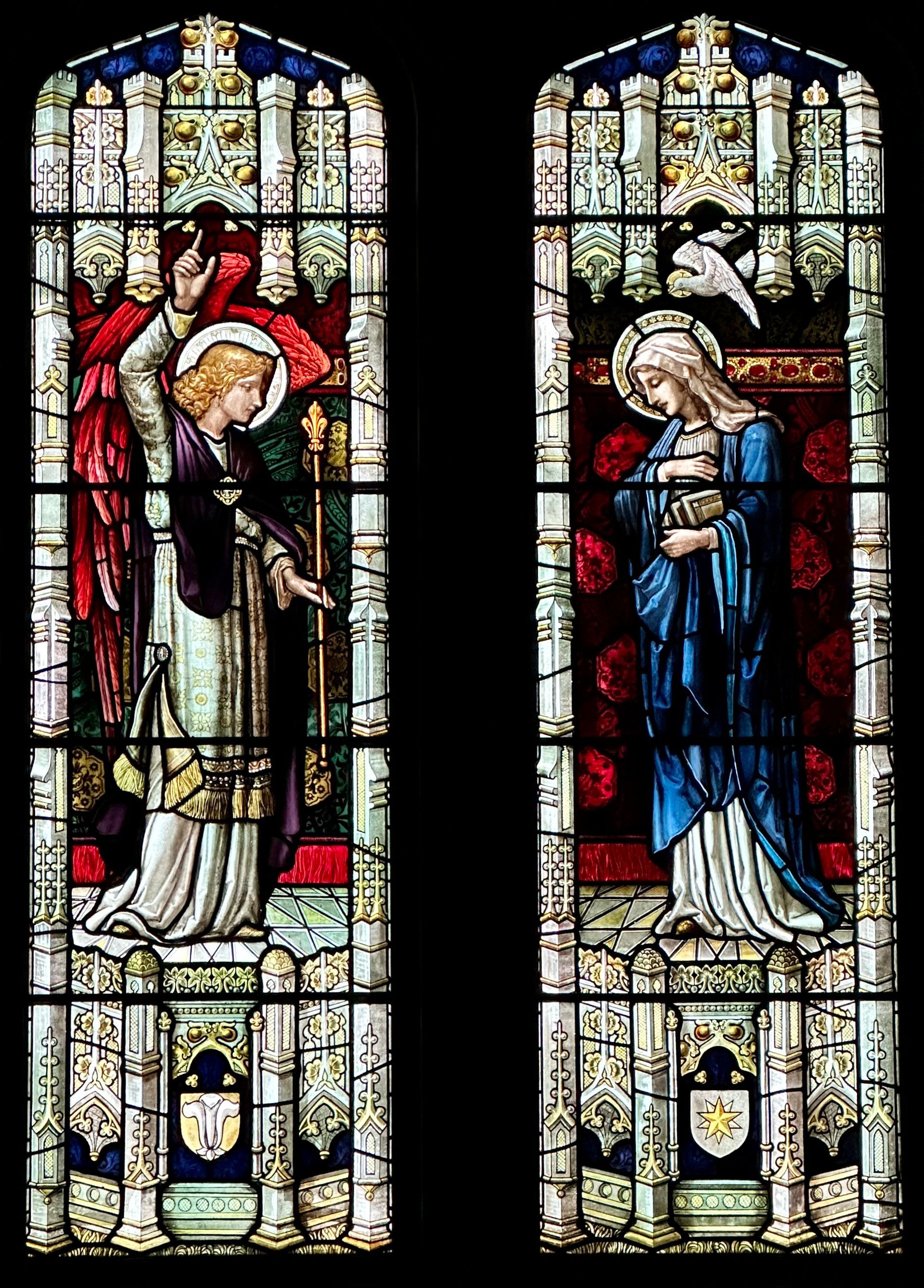 Stained glass panels: Angel Gabriel with Mary. The angel with red wings, Mary in blue, setting is a church.