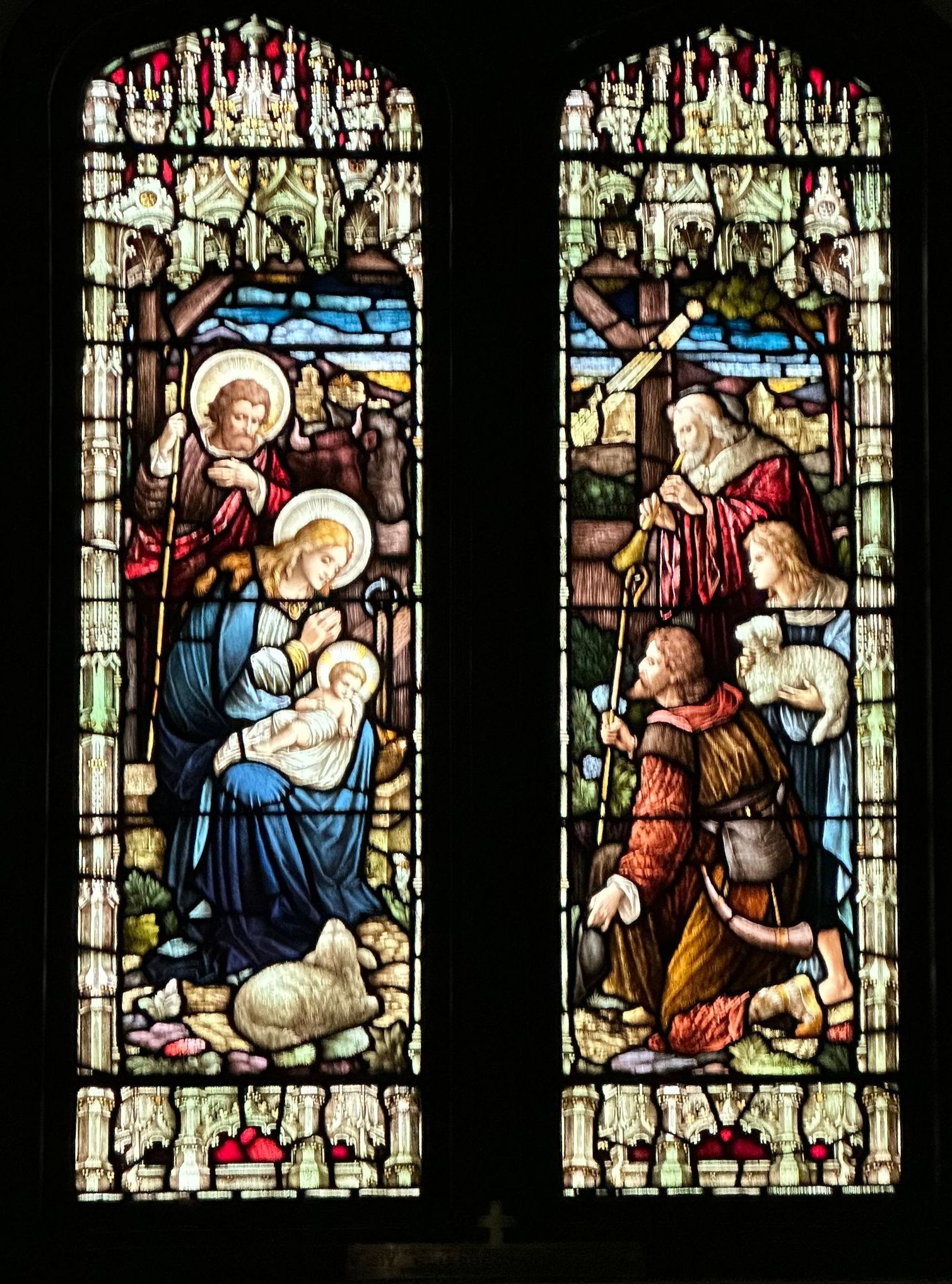 Stained glass windows depicting the Nativity scene: Mary with baby Jesus, Joseph, and shepherds kneeling.