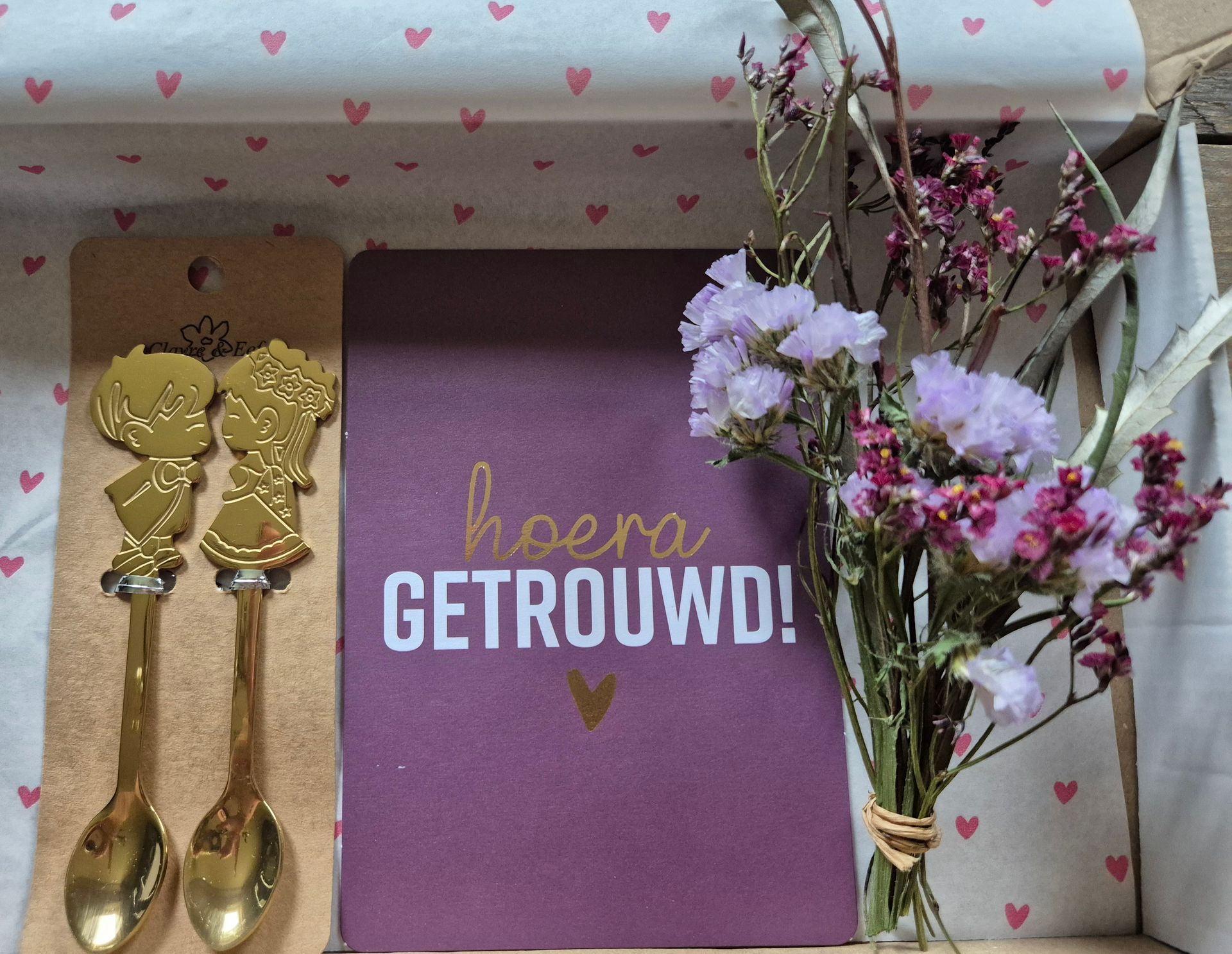 Cadeauverpakking met gouden lepels, bloemen en een paarse kaart met de tekst