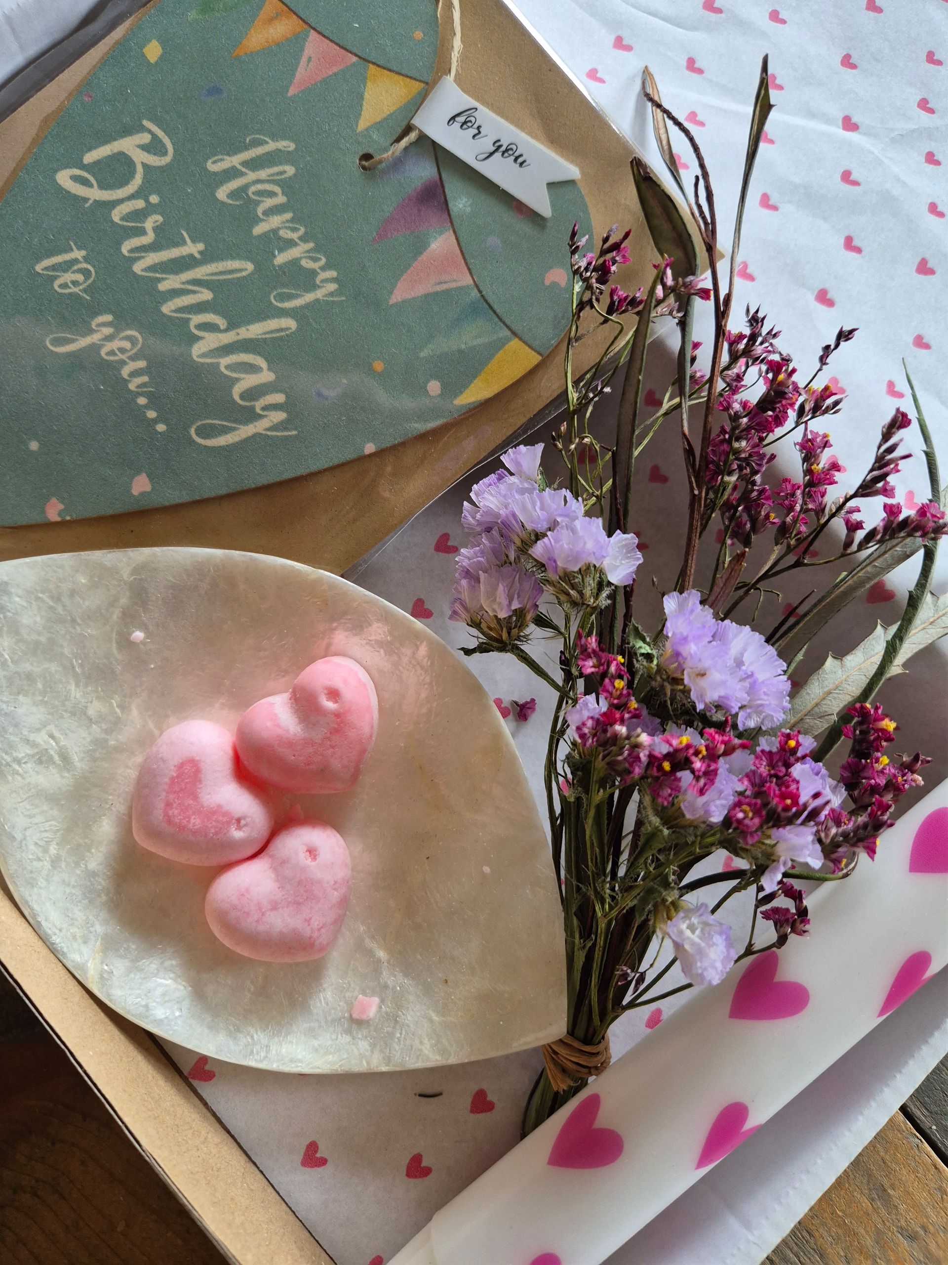 Verjaardagscadeauset met kaart, bloemen, roze kaarsen en hartvormige lekkernijen op een dienblad.