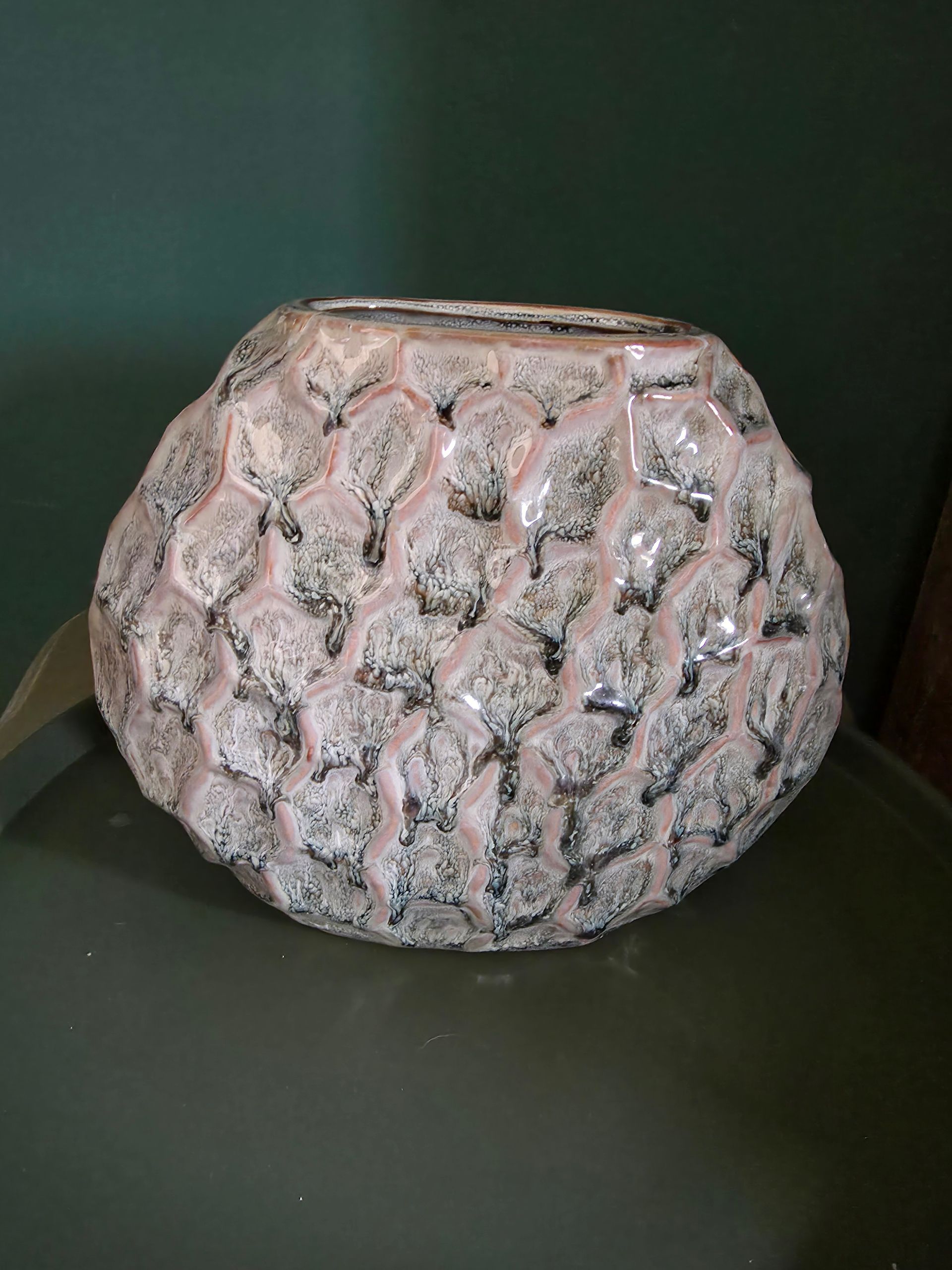 Een brandende kaars naast twee decoratieve pompoenen en een kom met structuur op een donker dienblad.