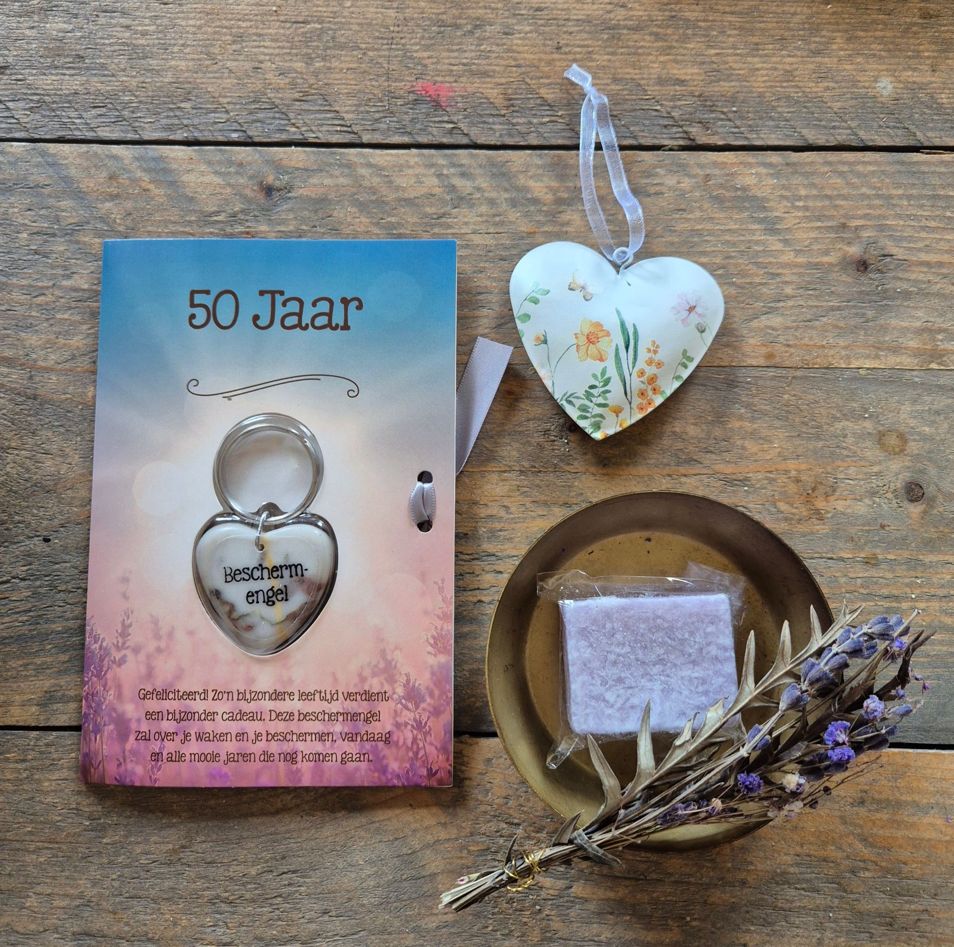 Cadeauset voor een 50e verjaardag met kaart, ringvormig voorwerp, gedroogde bloemen en hartvormig label op een achtergrond met stippen.