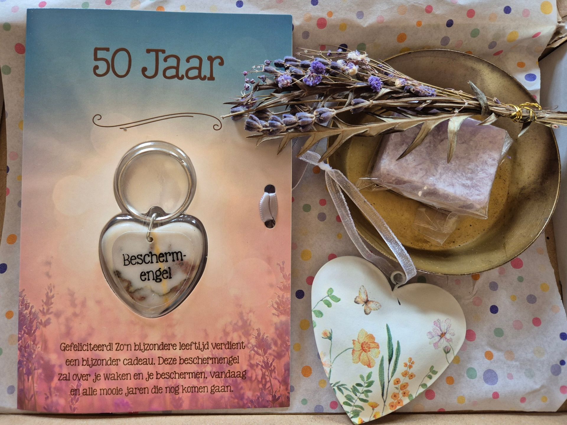 Cadeauset voor een 50e verjaardag met kaart, ringvormig voorwerp, gedroogde bloemen en hartvormig label op een achtergrond met stippen.