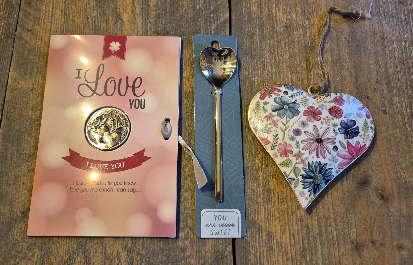 Valentijnscadeauset met roze kaart, lepel en doosje met bloemenhart op een houten tafel.