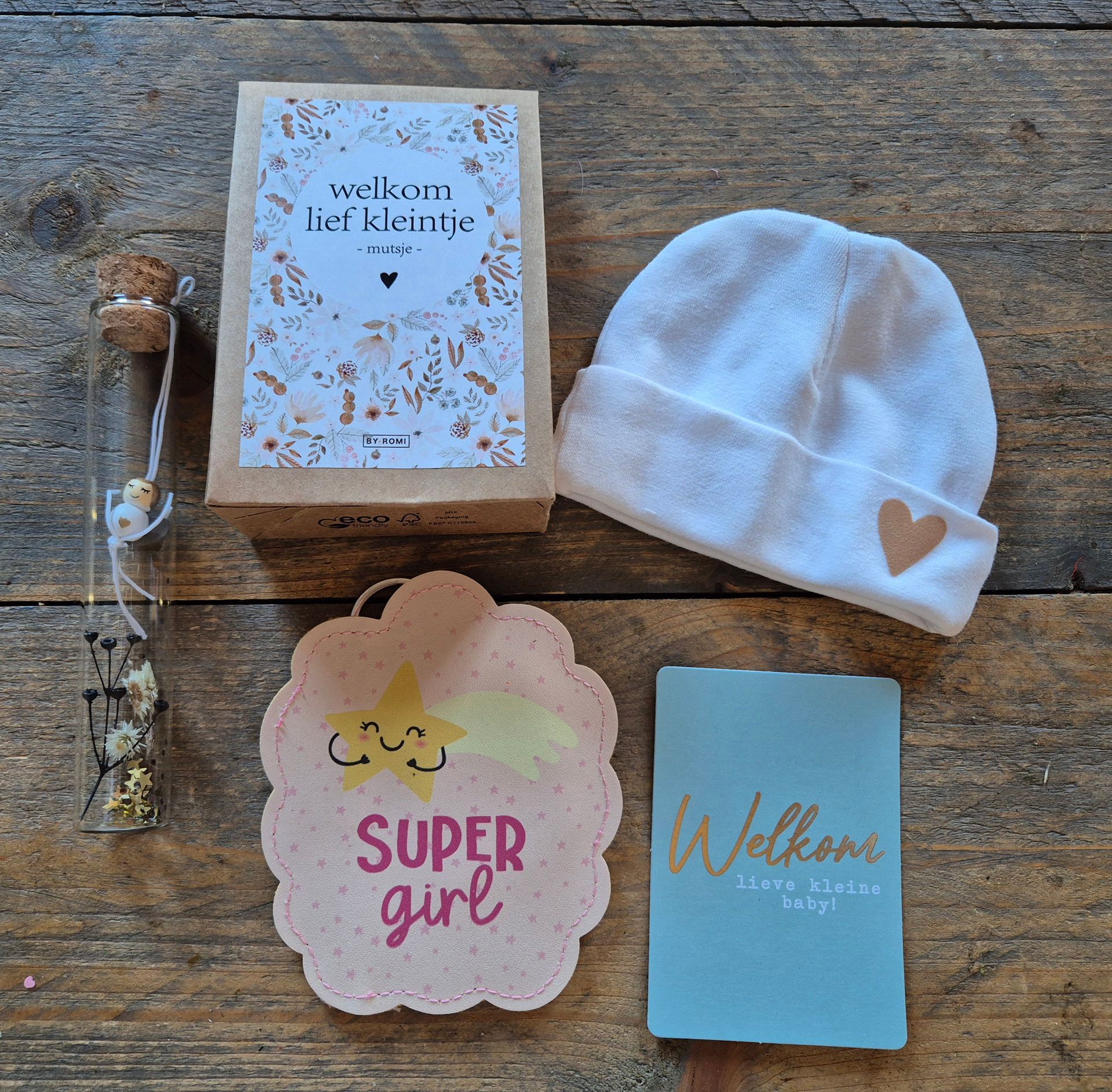 Babycadeauset op een houten tafeltje: dekentje, welkomstkaart, bordje