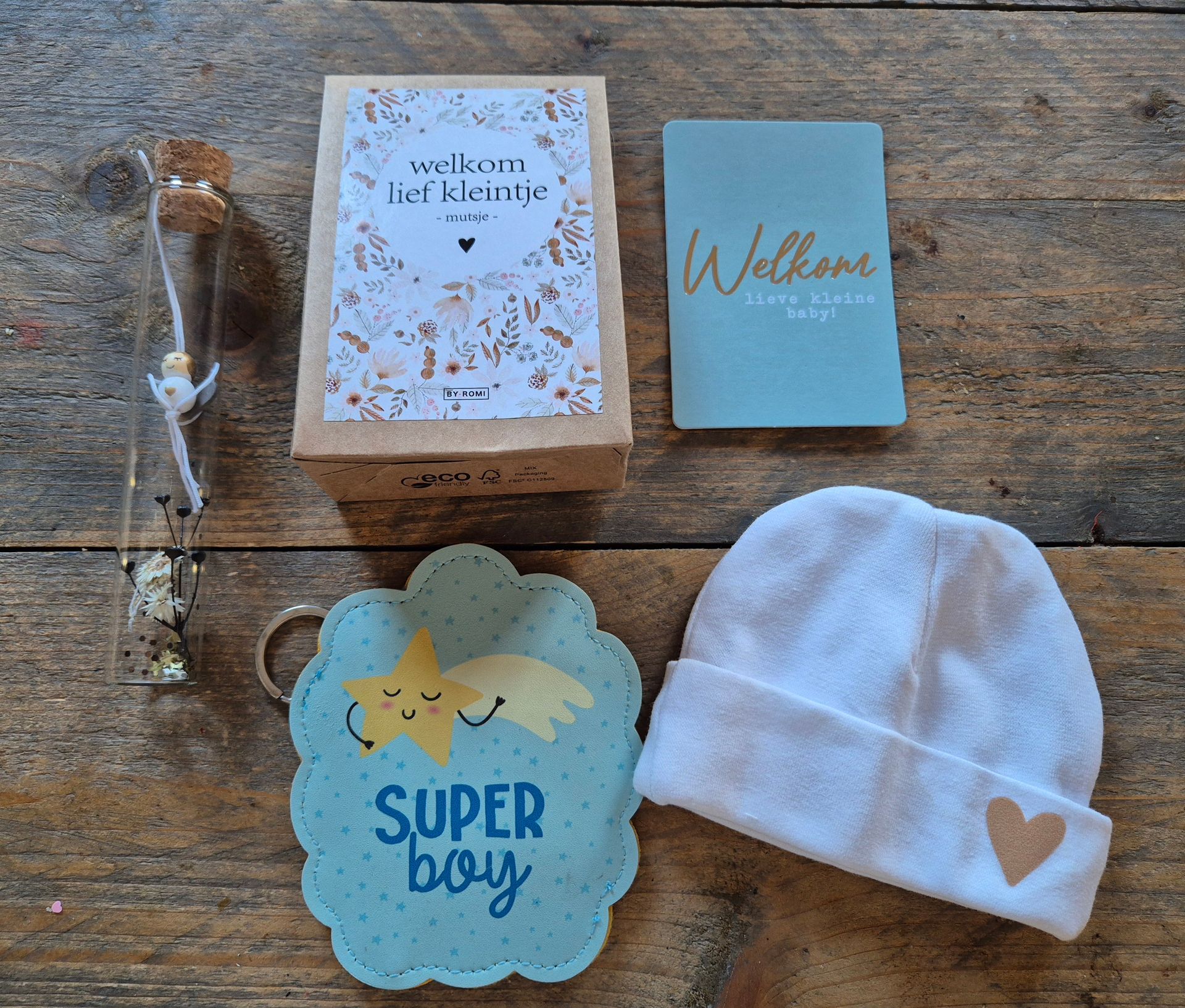 Babycadeauset op een houten tafeltje: dekentje, welkomstkaart, bordje