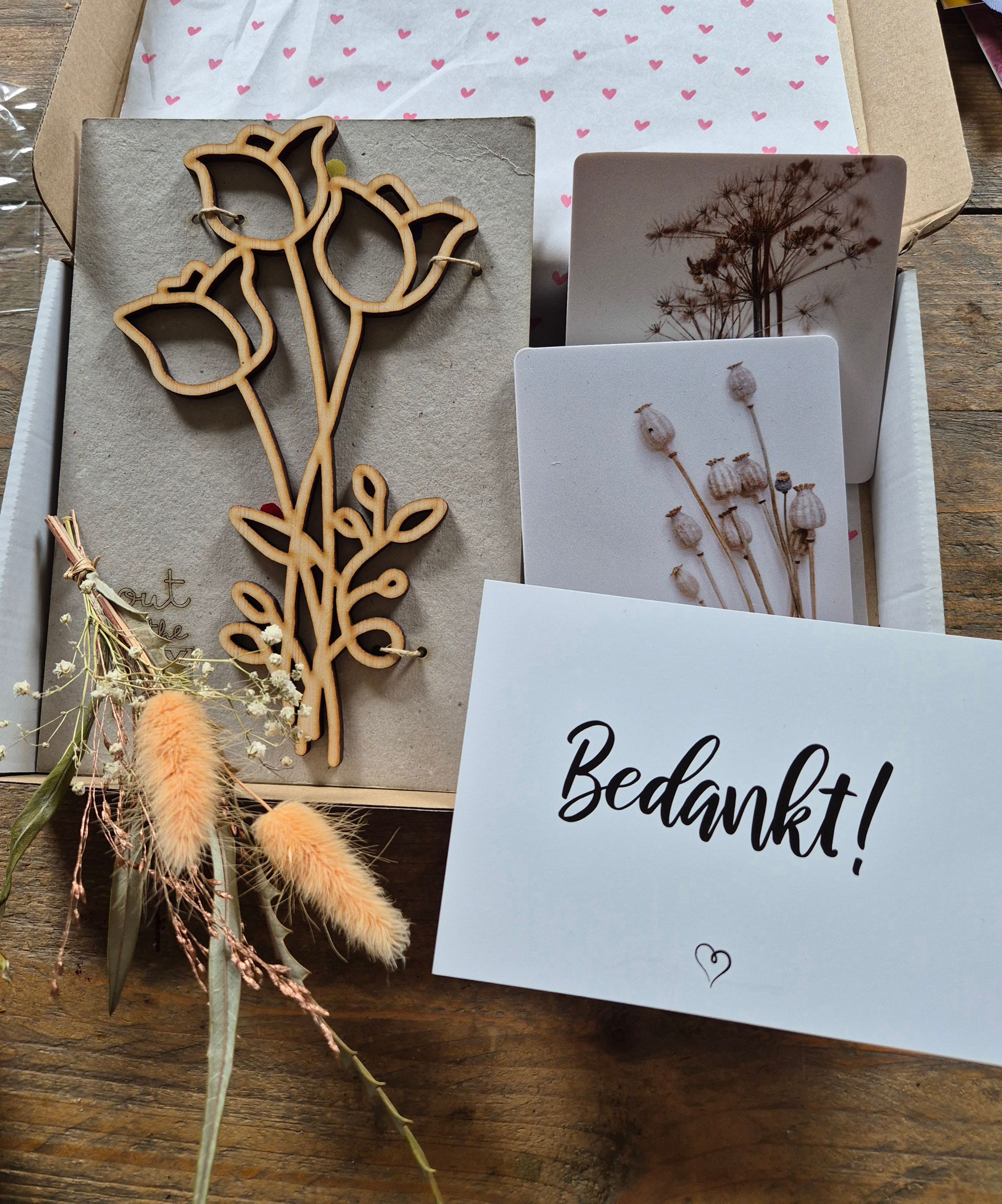 Handgemaakte bedankkaart met gedroogde bloemen en bloemmotieven op een rustieke houten tafel.