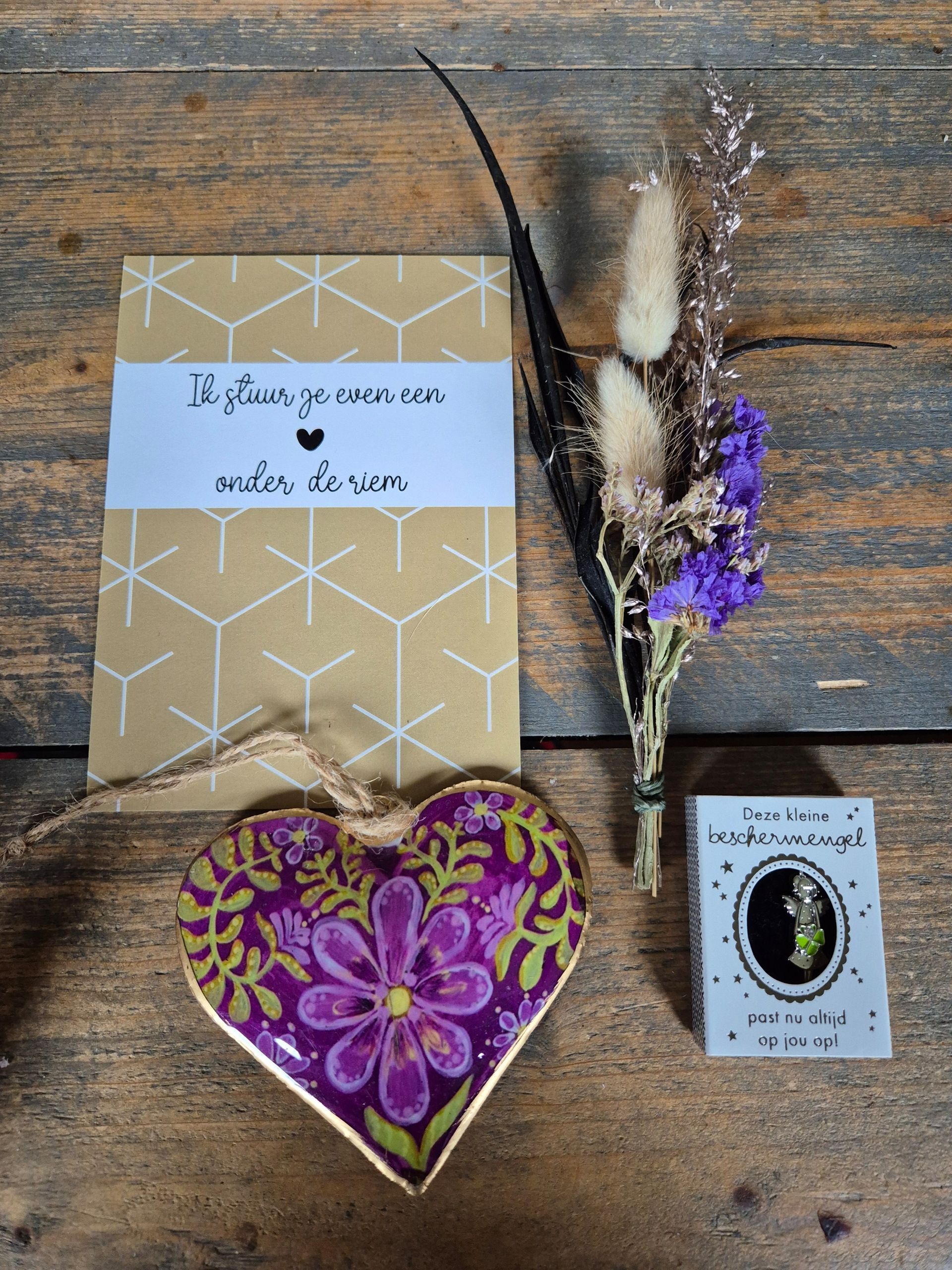 Cadeauverpakking met ingepakte artikelen, gedroogde bloemen en een paars hartvormig cadeautje onderin.