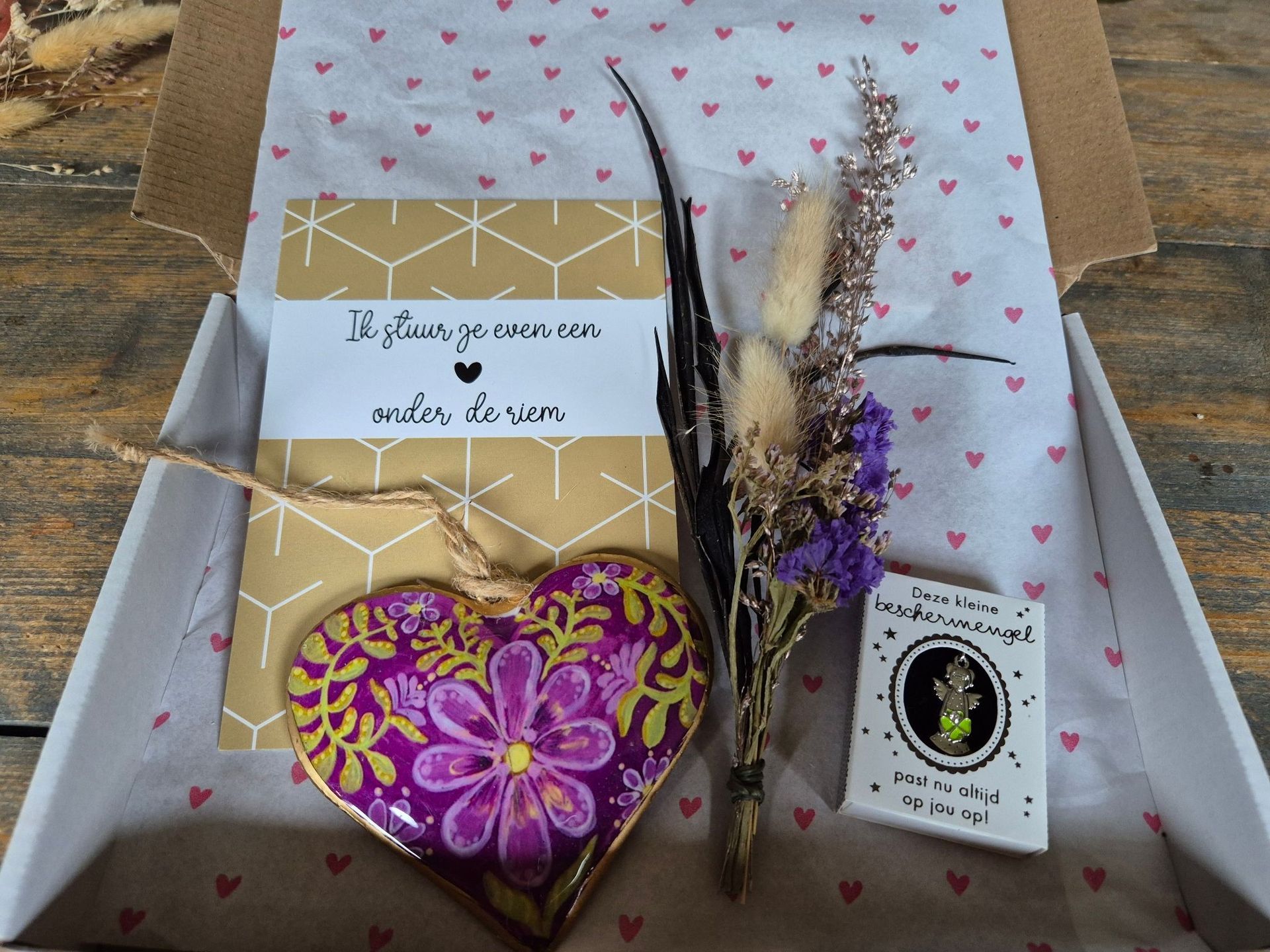Cadeauverpakking met ingepakte artikelen, gedroogde bloemen en een paars hartvormig cadeautje onderin.