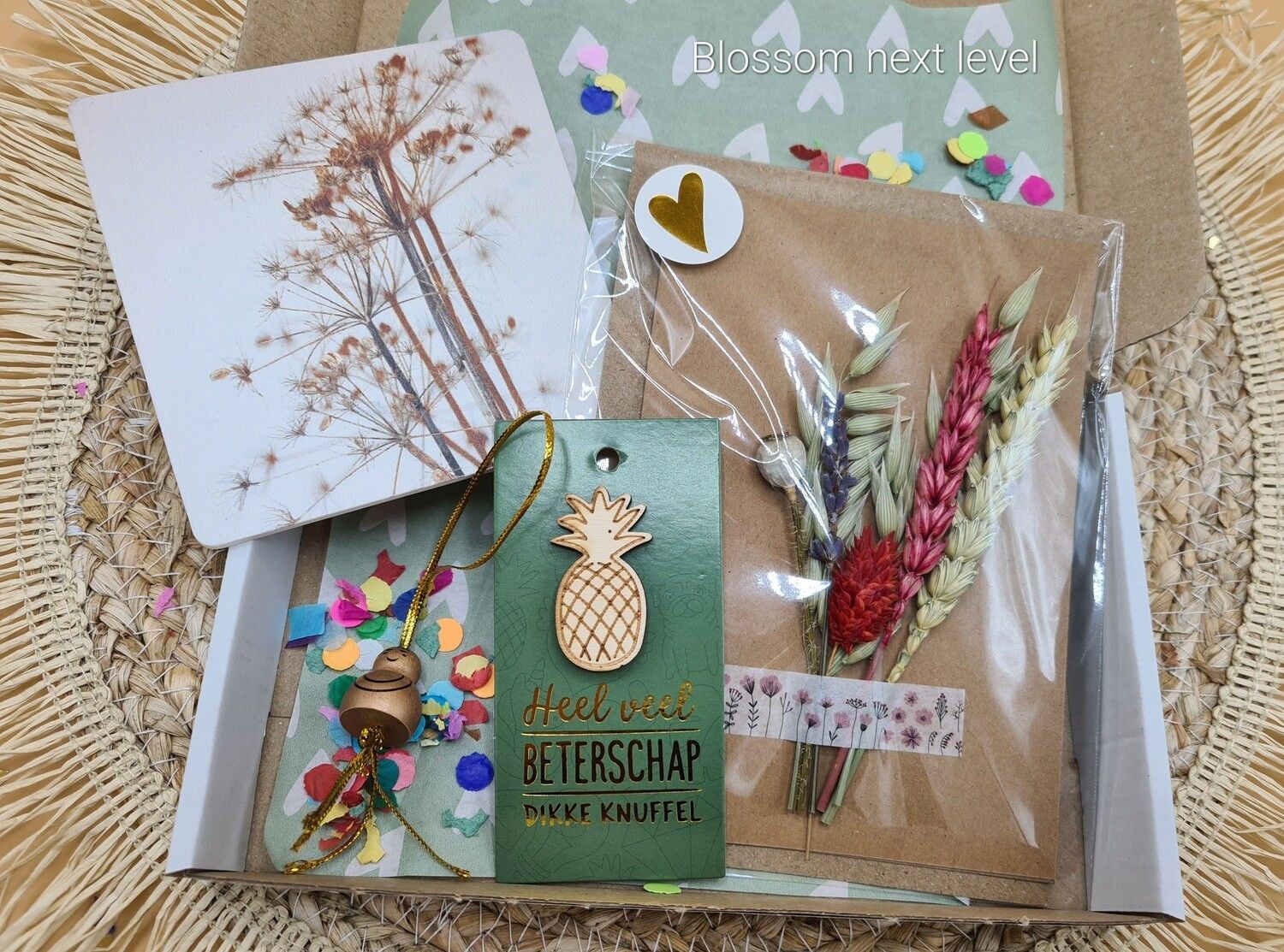 Handgemaakte wenskaart met gedroogde bloemen, gouden accenten en een klein label op een achtergrond van kraftpapier.