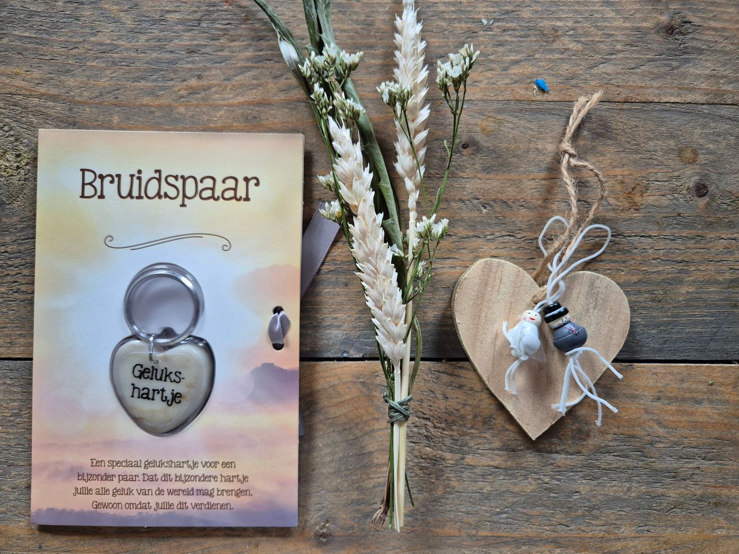 Bruidspaar cadeaukaart met zilveren hartvormige sleutelhanger, gedroogde bloemen en een klein kaarsje op een achtergrond met patroon.