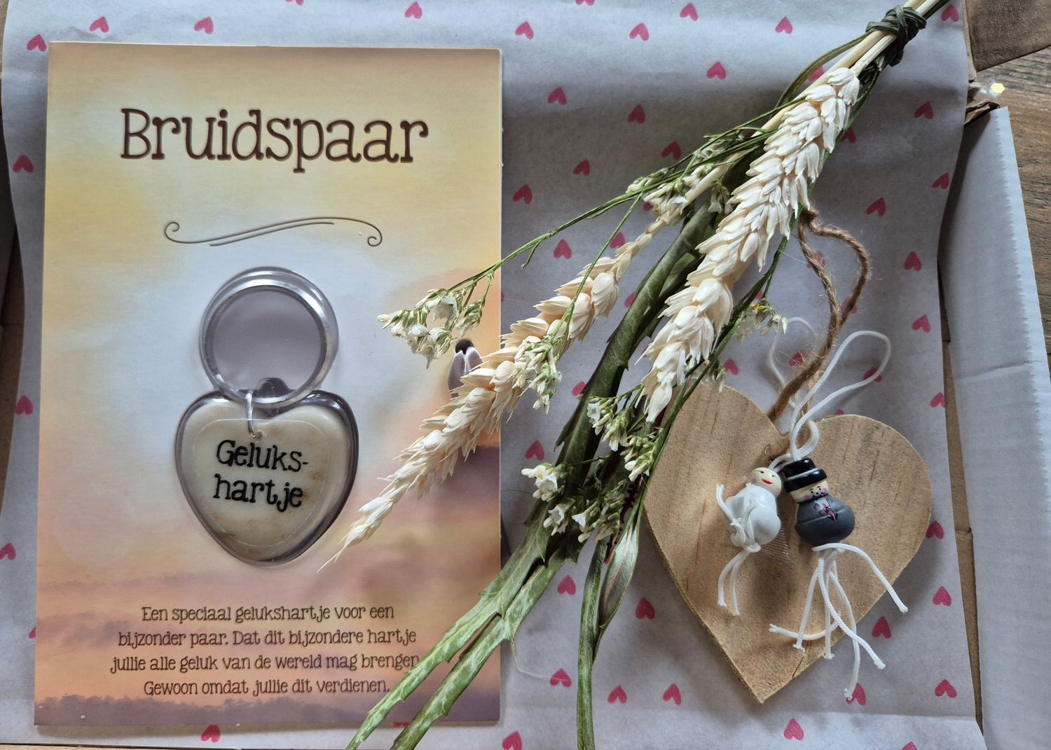 Bruidspaar cadeaukaart met zilveren hartvormige sleutelhanger, gedroogde bloemen en een klein kaarsje op een achtergrond met patroon.