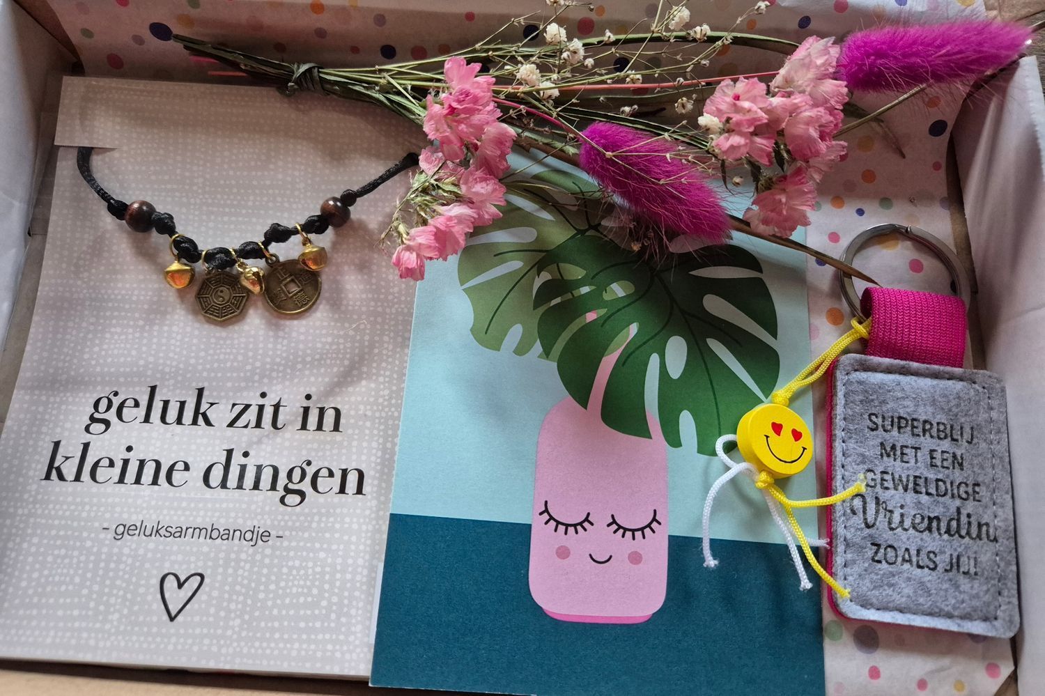 Cadeauverpakking met bloemen, een armband, een tekening van een roze vaas en kaartjes met Nederlandse tekst op wit en turquoise papier.