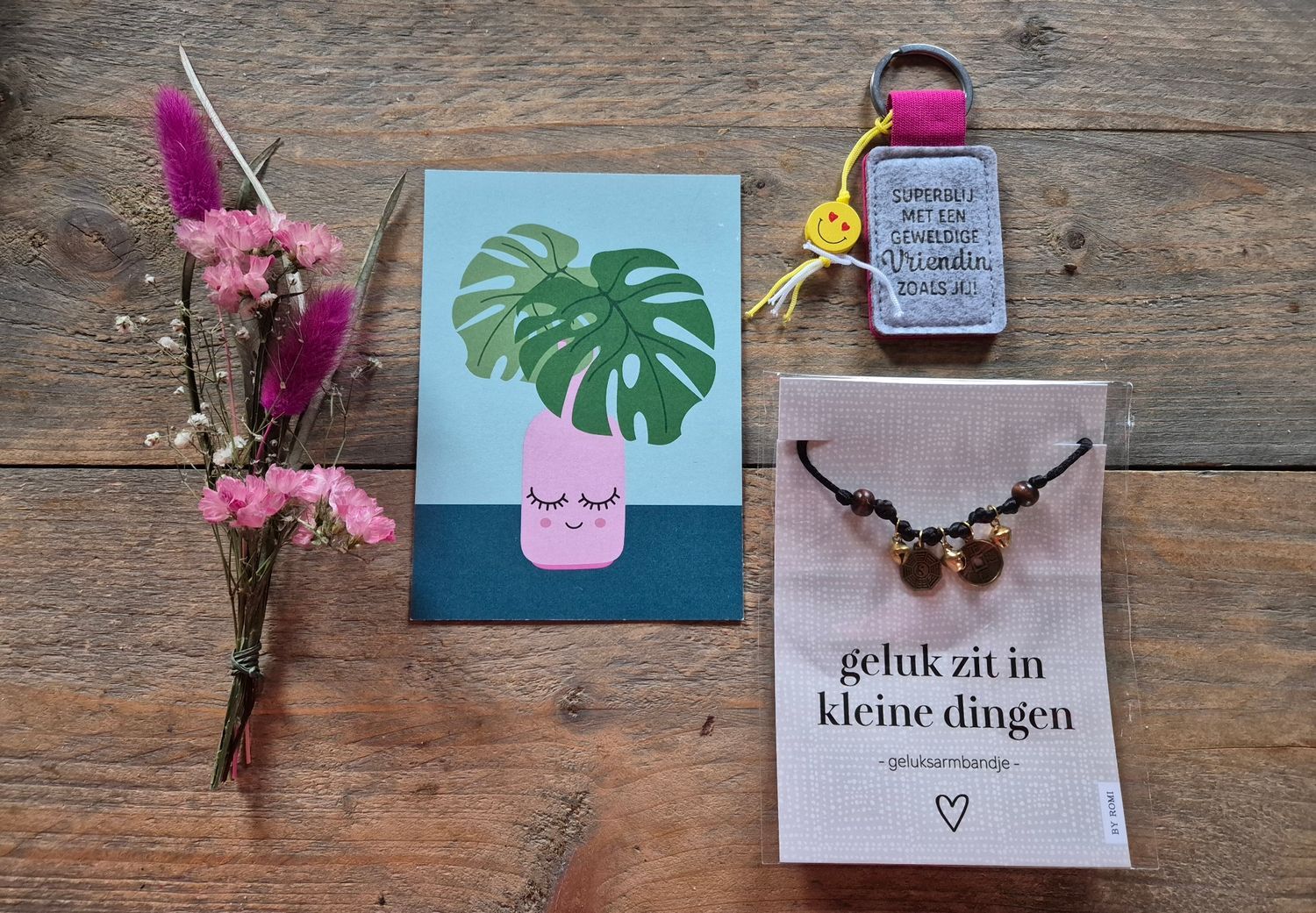 Cadeauverpakking met bloemen, een armband, een tekening van een roze vaas en kaartjes met Nederlandse tekst op wit en turquoise papier.