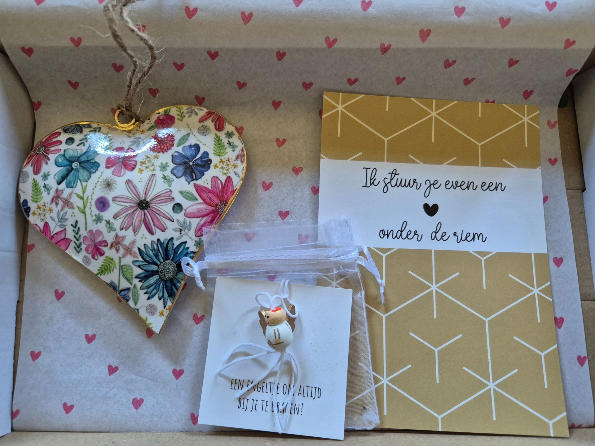 Drie handgemaakte cadeautjes op een houten ondergrond: een hartvormig ornament met bloemen, een klein zakje en een gouden kaartje.