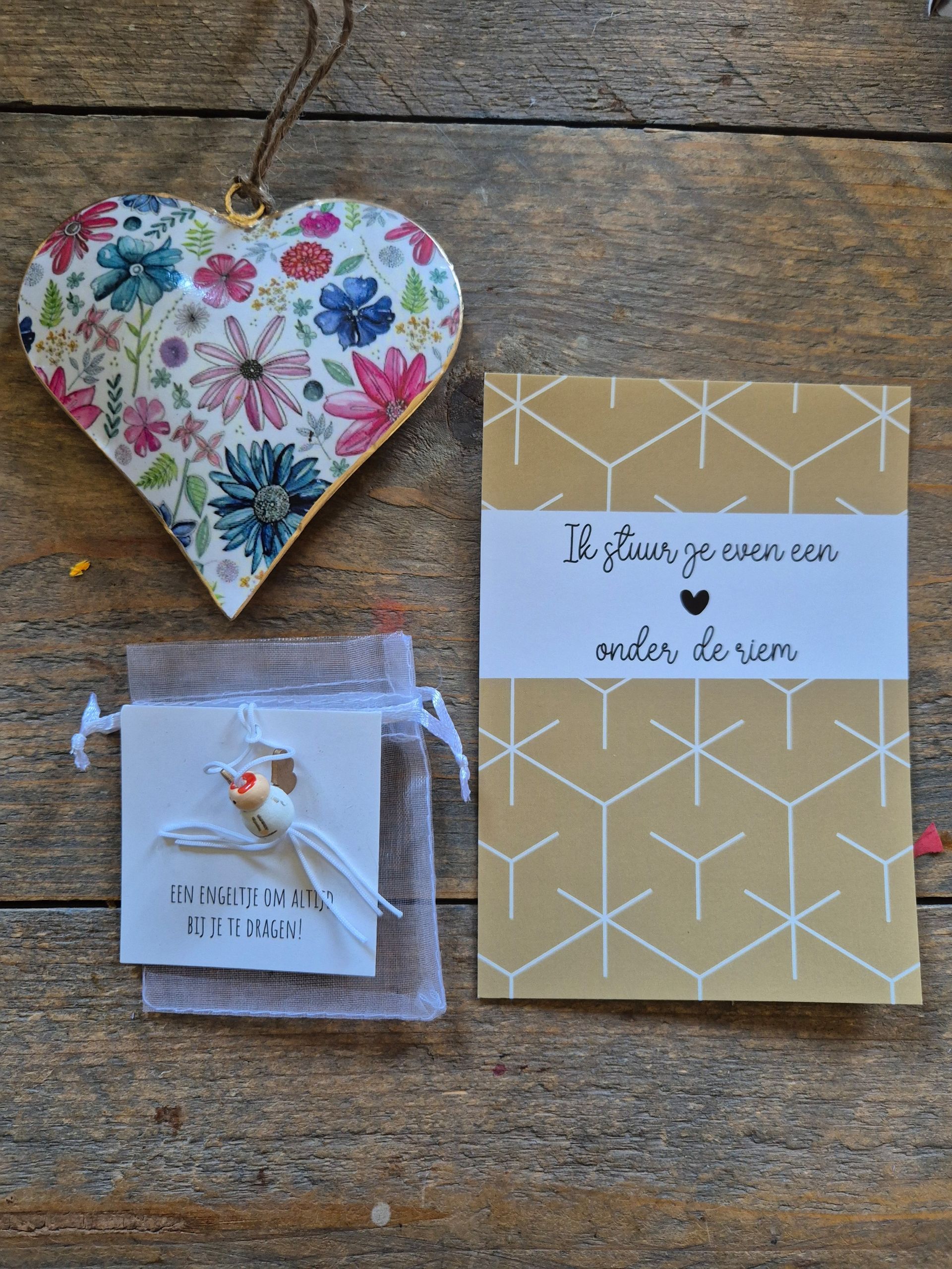 Drie handgemaakte cadeautjes op een houten ondergrond: een hartvormig ornament met bloemen, een klein zakje en een gouden kaartje.