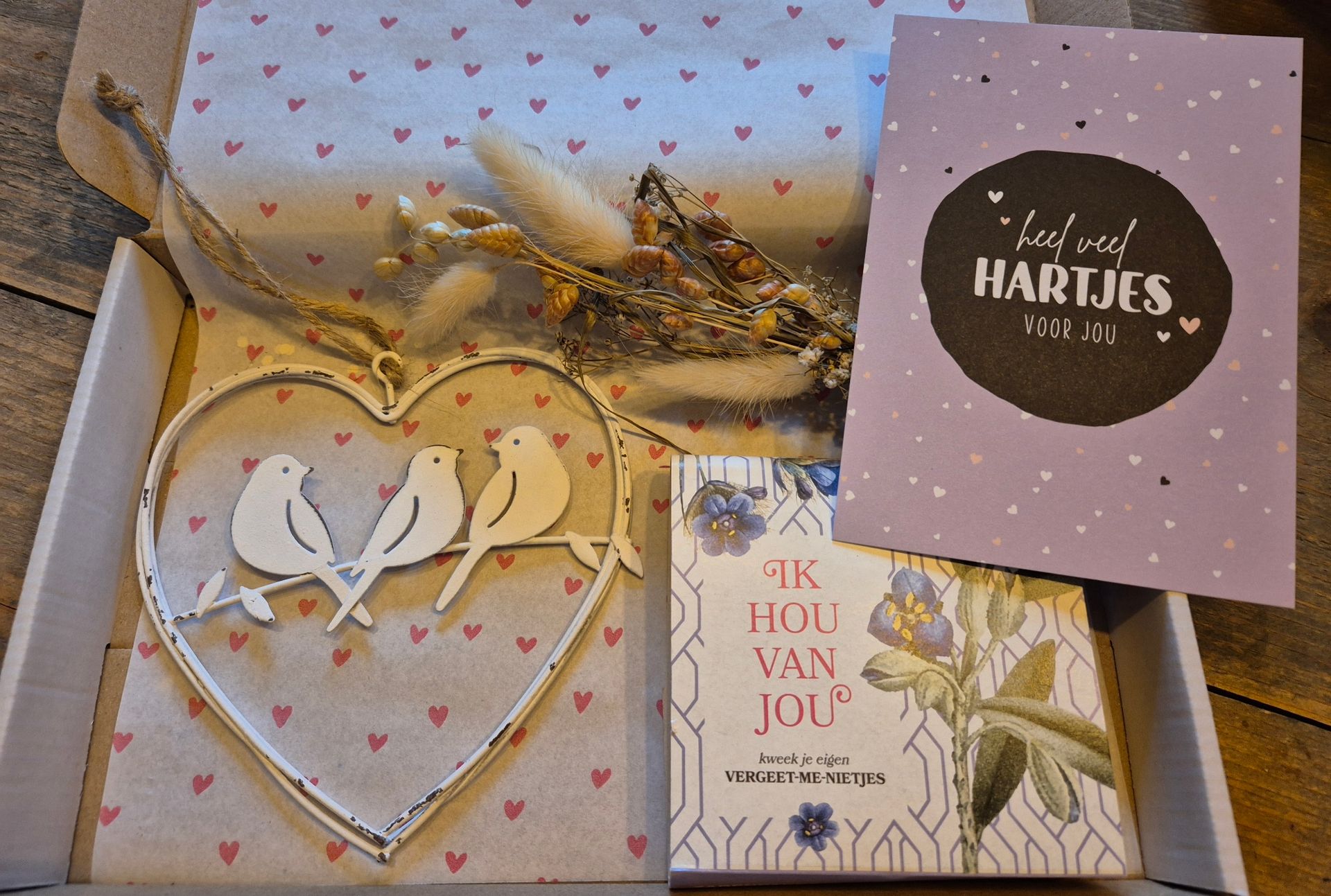 Cadeauverpakking met hartvormige ornamenten, takjes als decoratie en twee wenskaarten op bedrukt papier.