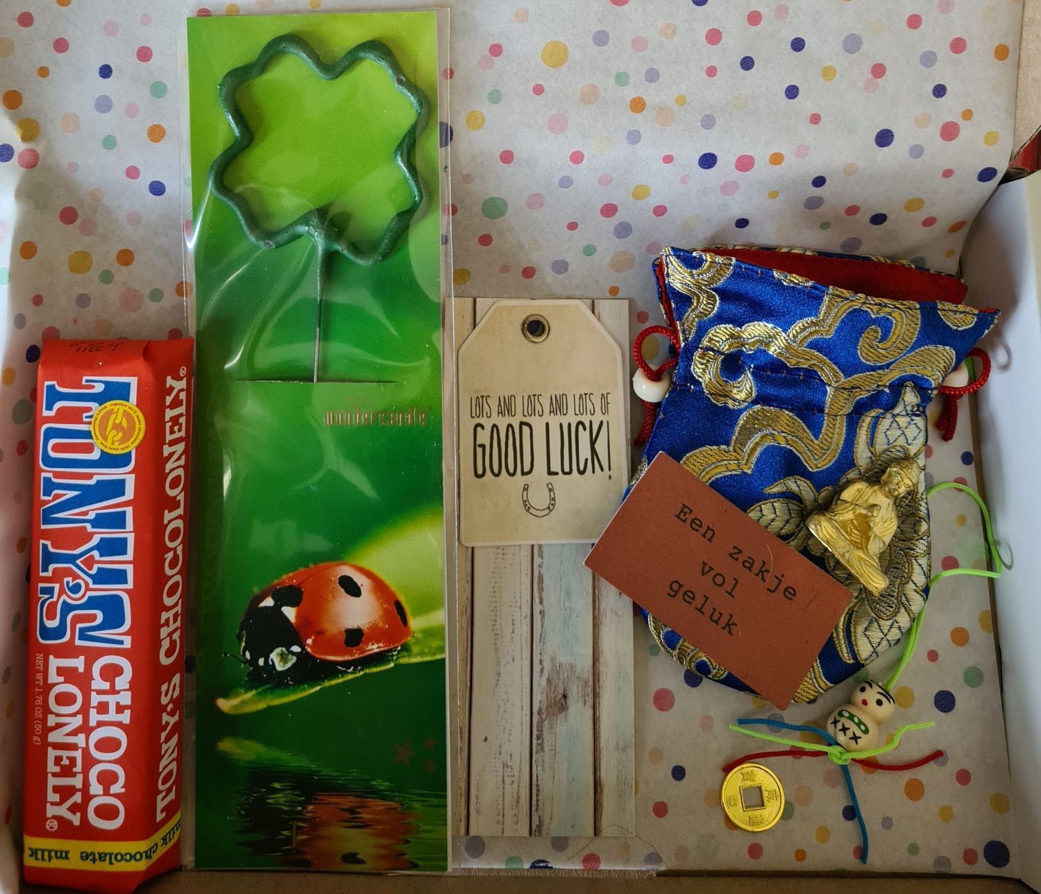 Cadeaumand met een klaverballon, snoep, een lieveheersbeestje en gelukswensen, verpakt in inpakpapier met stippen.
