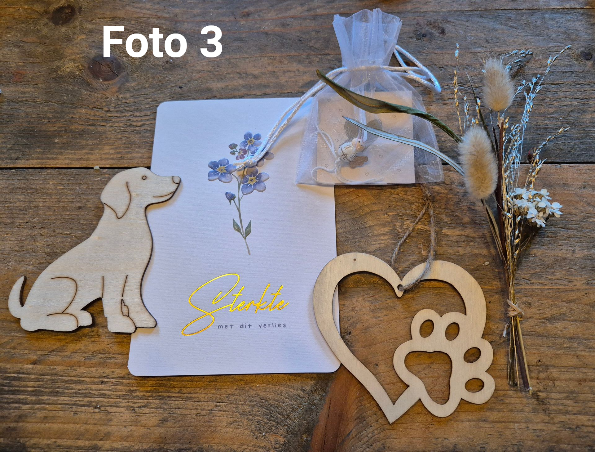 Houten katten- en hartornamenten met een witte geschenkdoos en gedroogde bloemen op een rustieke tafel.