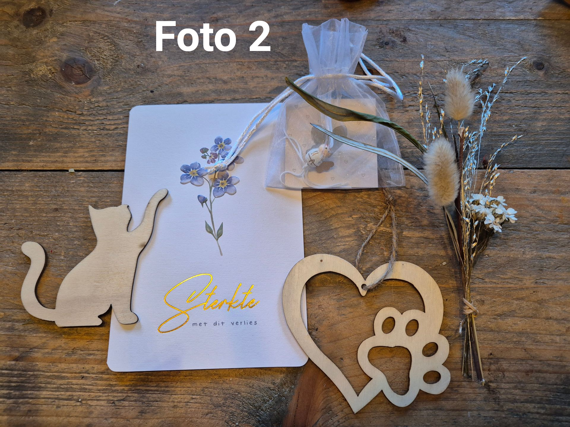 Houten katten- en hartornamenten met een witte geschenkdoos en gedroogde bloemen op een rustieke tafel.