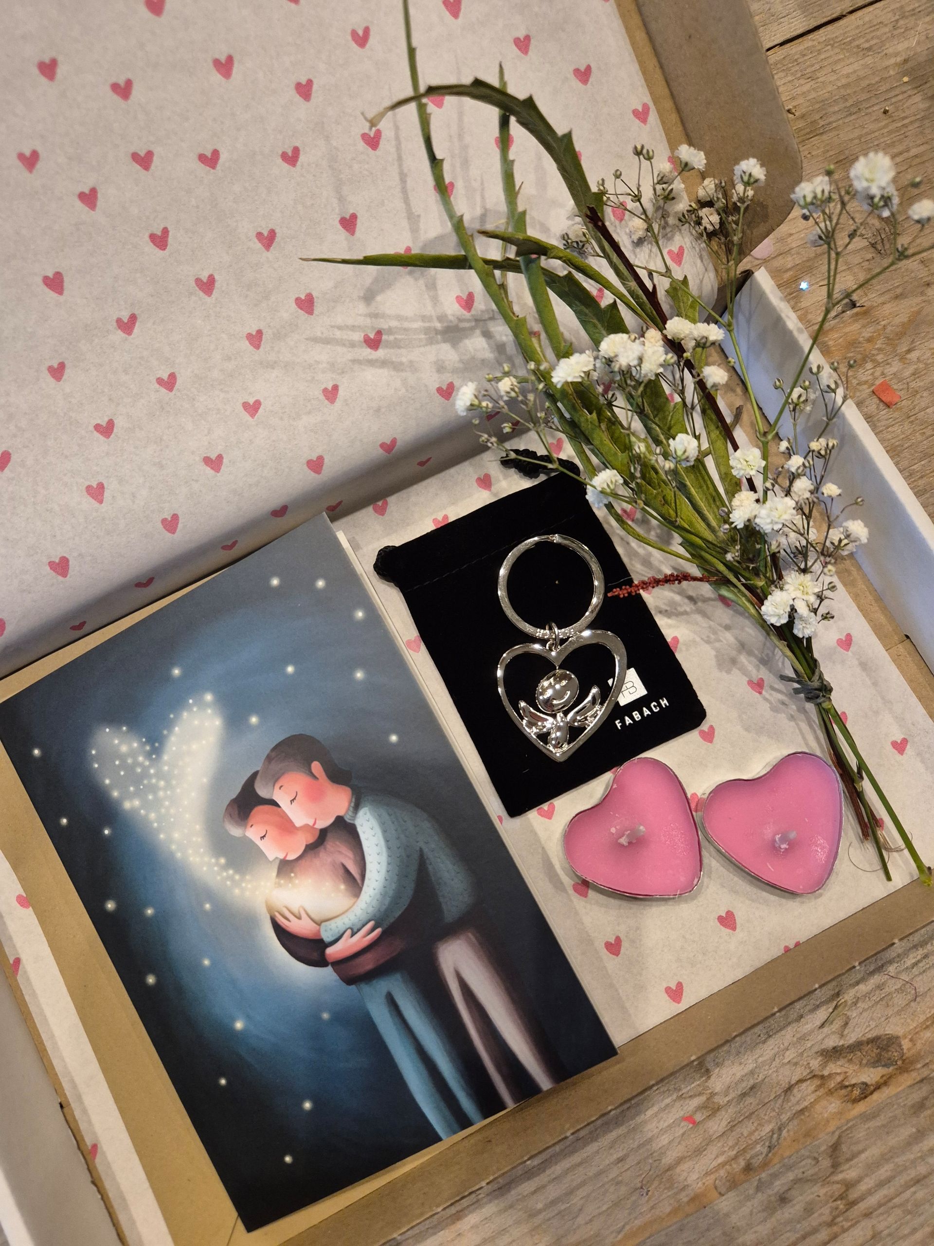 Romantische afbeelding met een omhelzend stel, zilveren hartvormige sieraden en roze hartvormige decoratie op een lichte achtergrond.