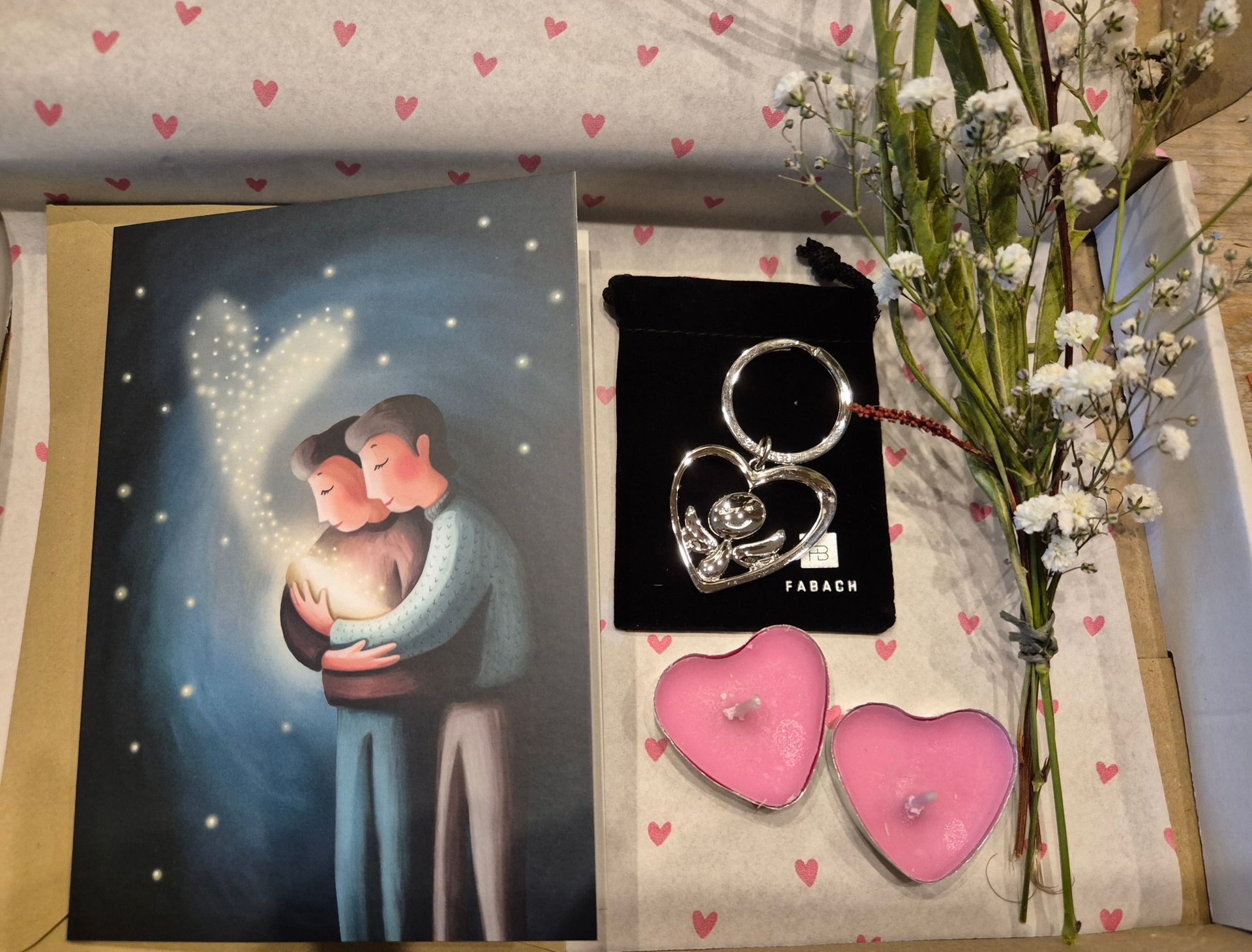 Romantische afbeelding met een omhelzend stel, zilveren hartvormige sieraden en roze hartvormige decoratie op een lichte achtergrond.