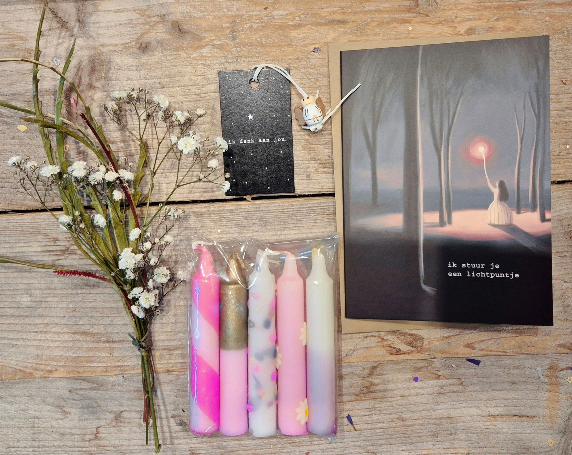 Cadeauverpakking met roze kaarsen, gedroogde bloemen en twee geïllustreerde kaarten met een zonsondergang en een sterrenhemel.