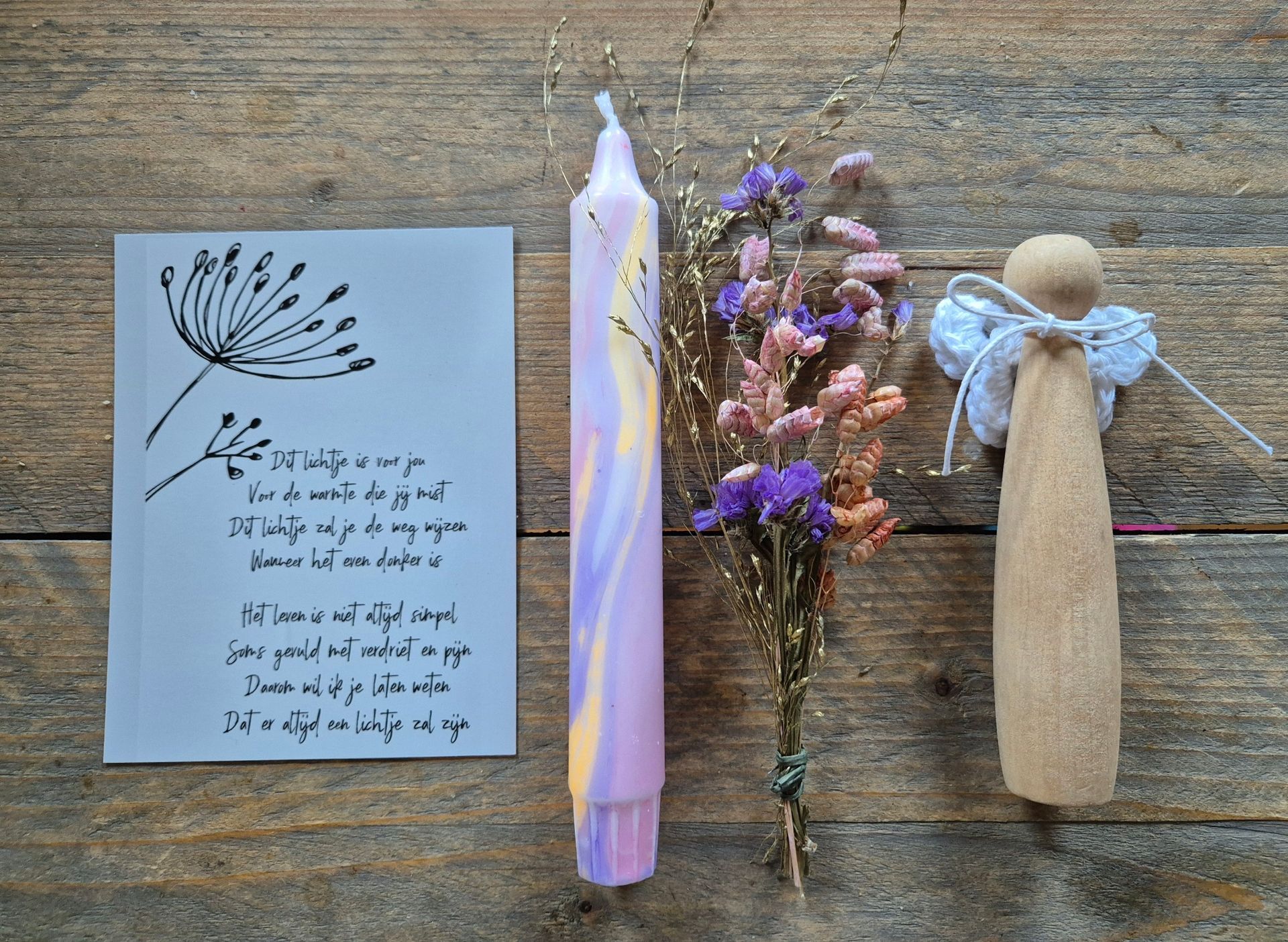 Notitieboekpagina, pastelkleurige kaars, gedroogde bloemen en houten pop op een rustieke houten ondergrond.