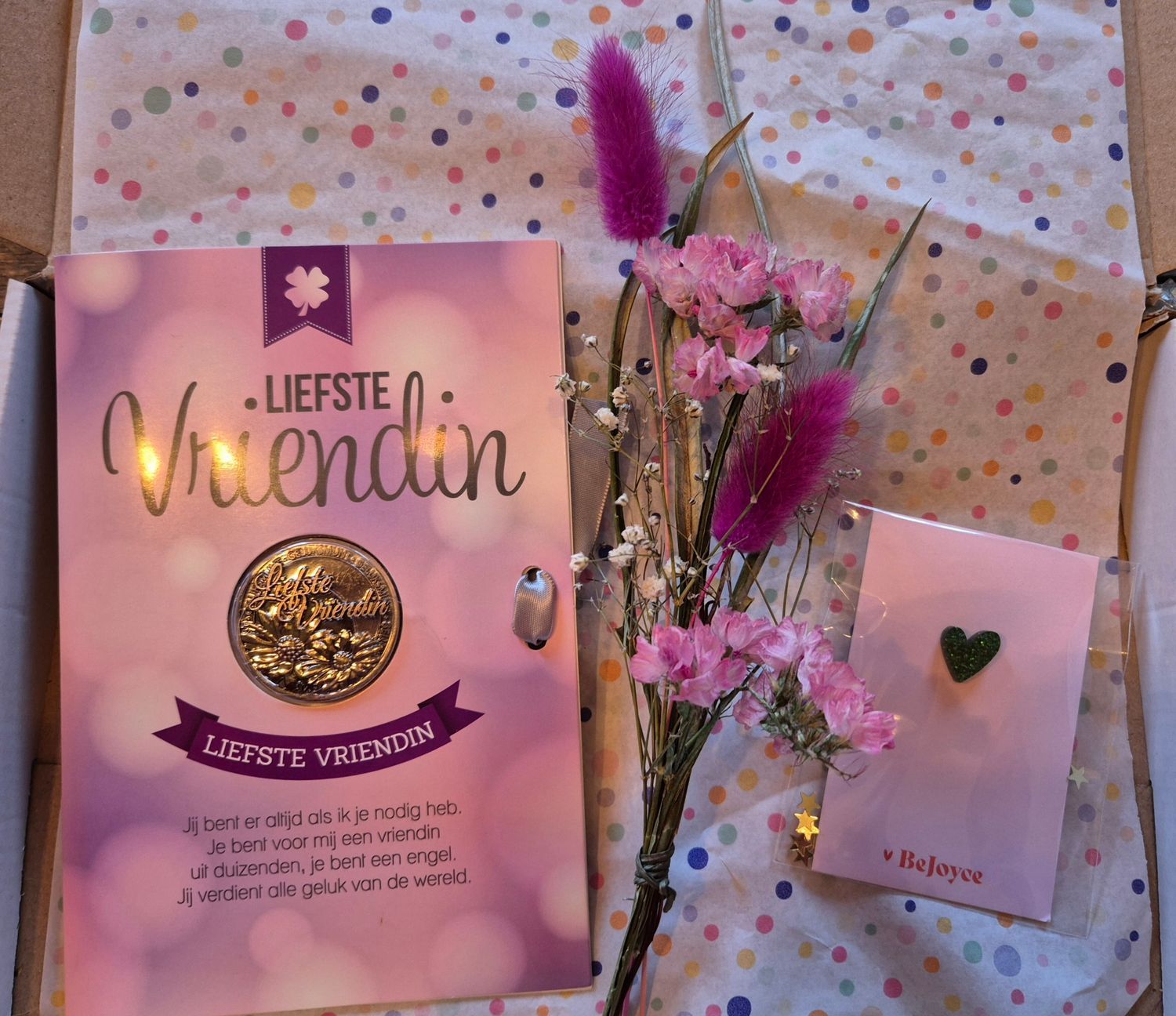 Roze cadeautasje en kaartje voor “Liefste vriendin” met bloemen en een gouden medaillon op ingepakt papier met stippen.