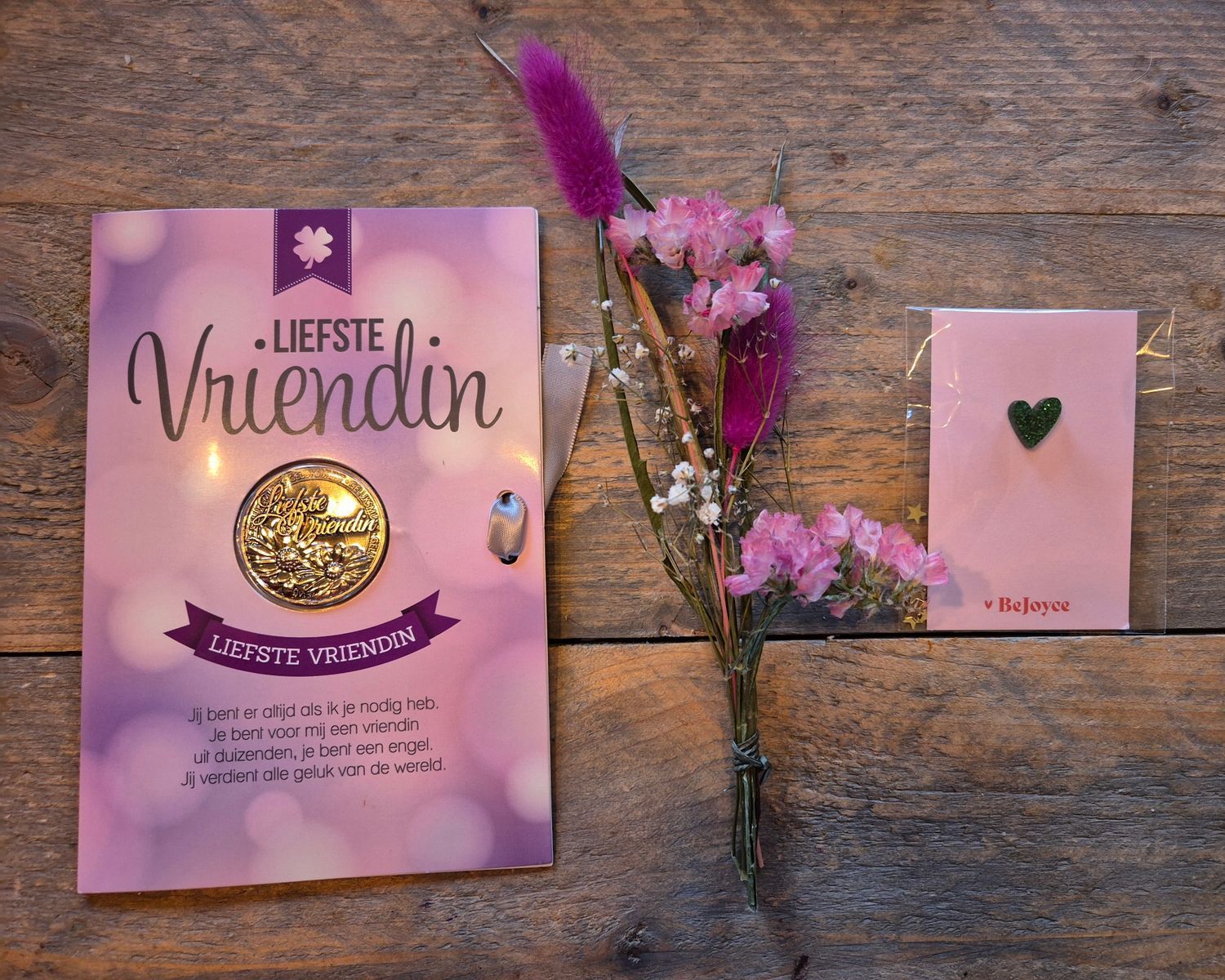 Roze cadeautasje en kaartje voor “Liefste vriendin” met bloemen en een gouden medaillon op ingepakt papier met stippen.