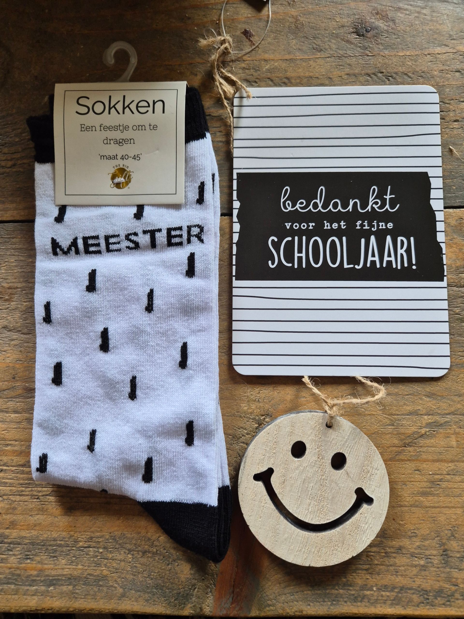 Gift set with socks, “meester” sign, “bedankt schooljaar!” card, and smiley ornament on a polka-dot background