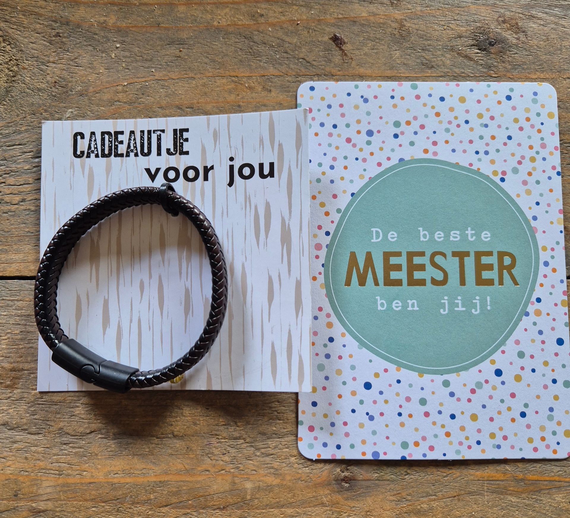 Bracelet beside two Dutch gift cards on a wooden surface, one reading “cadeautje voor jou” and “De beste meester ben jij!”