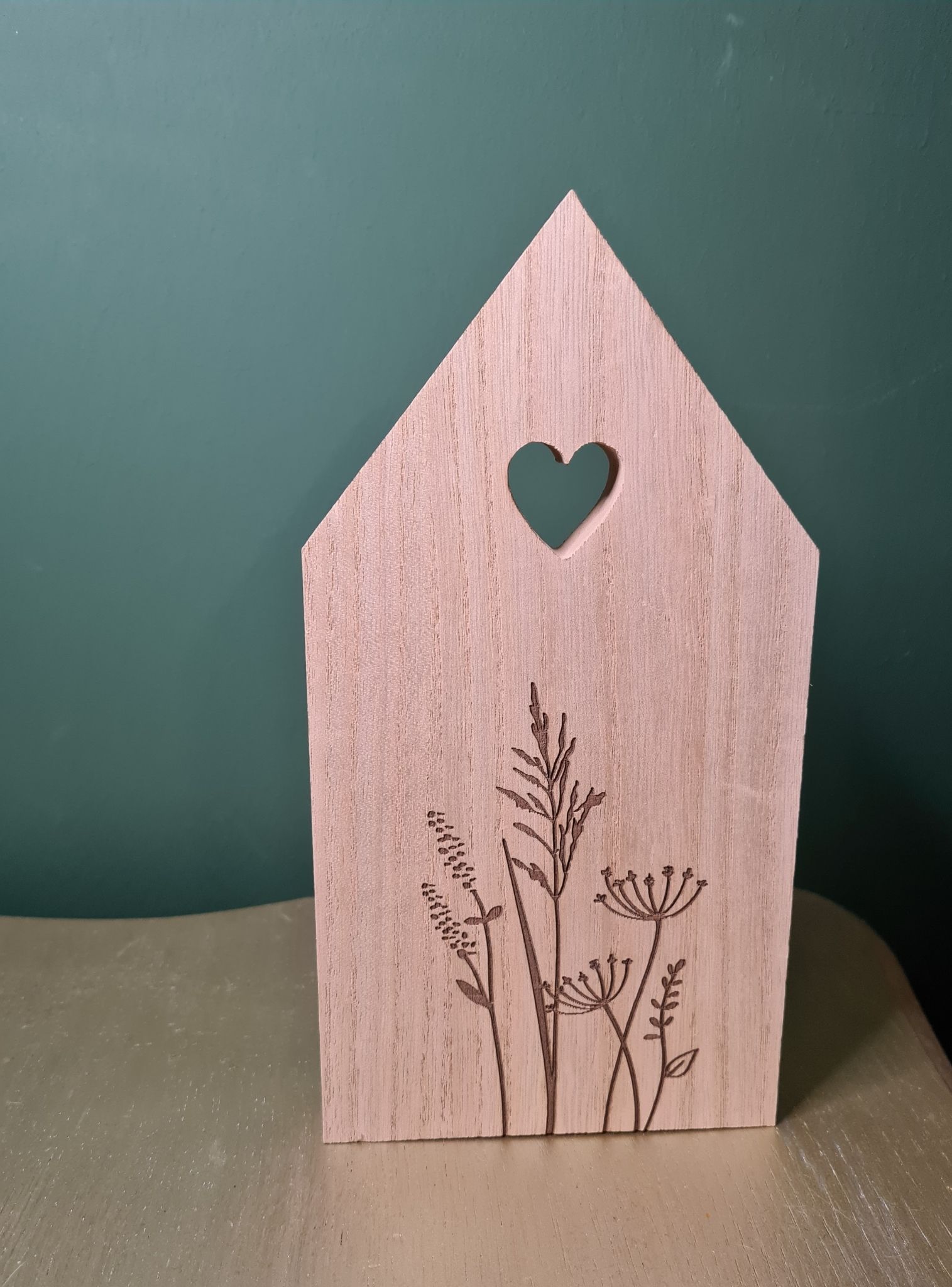 Houten decoratie in de vorm van een huisje met een hartvormige uitsparing en gedroogde bloemen naast een klein