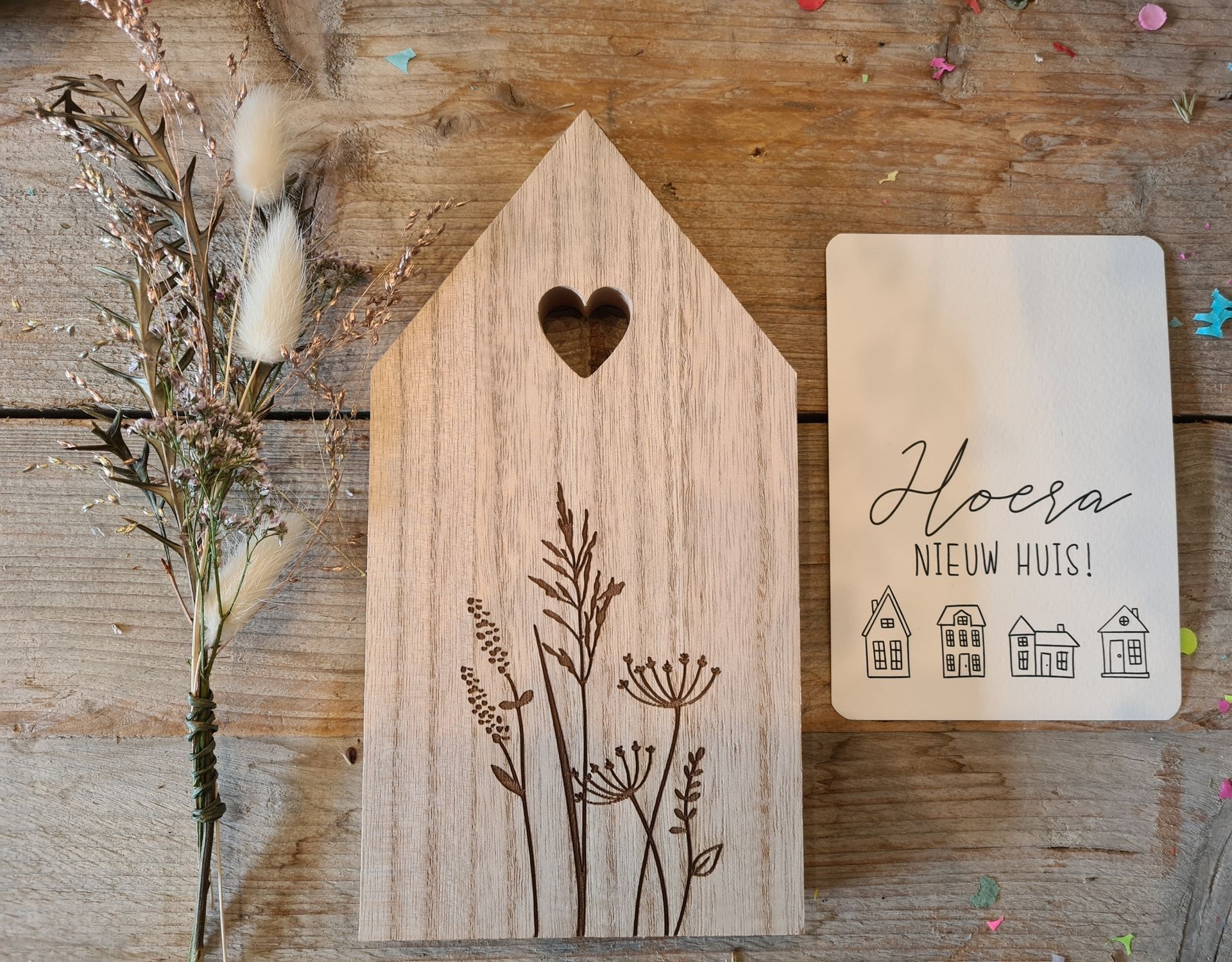 Houten decoratie in de vorm van een huisje met een hartvormige uitsparing en gedroogde bloemen naast een klein