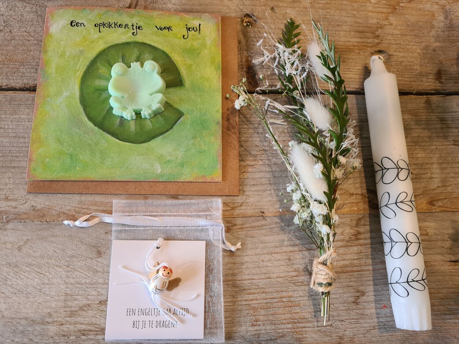 Groene cadeauset met bloemenmotief, inclusief kaart, gedroogde bloemen en opgerold papier op een tafel.